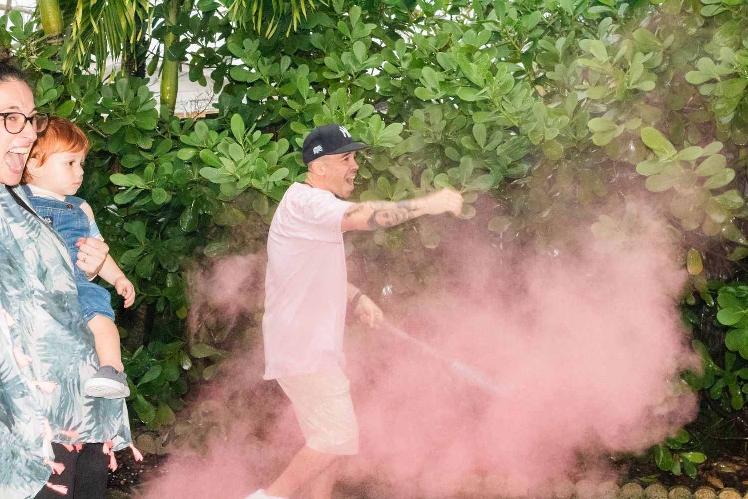 Gender reveal party moment captured with pink smoke effect in garden setting.