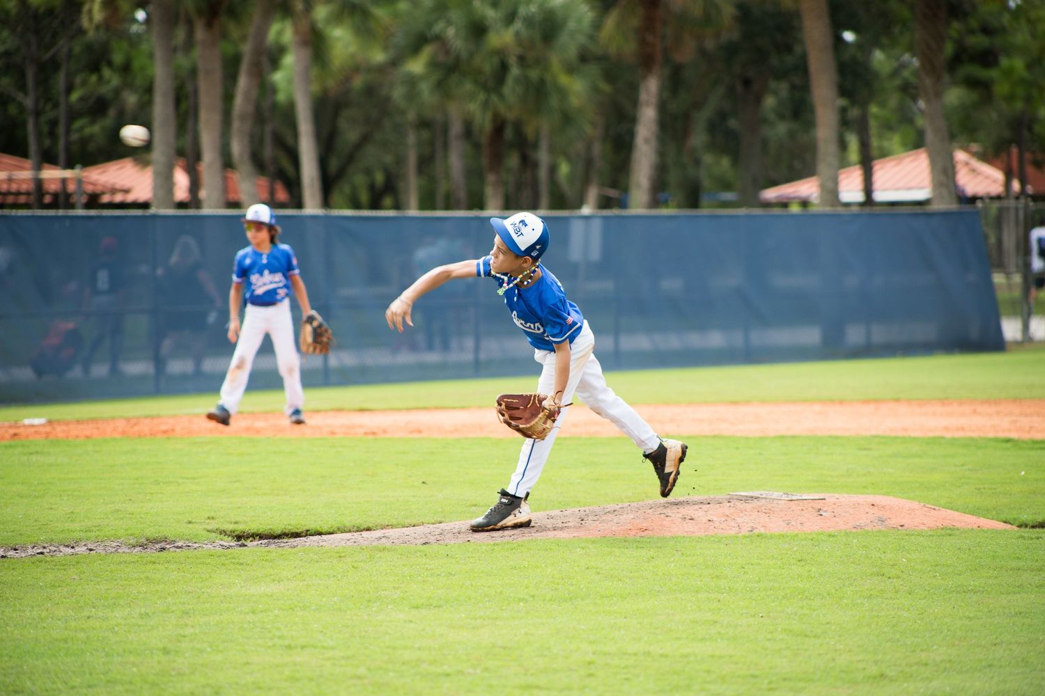 Youth baseball pitcher in mid-throwing motion on a well-maintained baseball field.