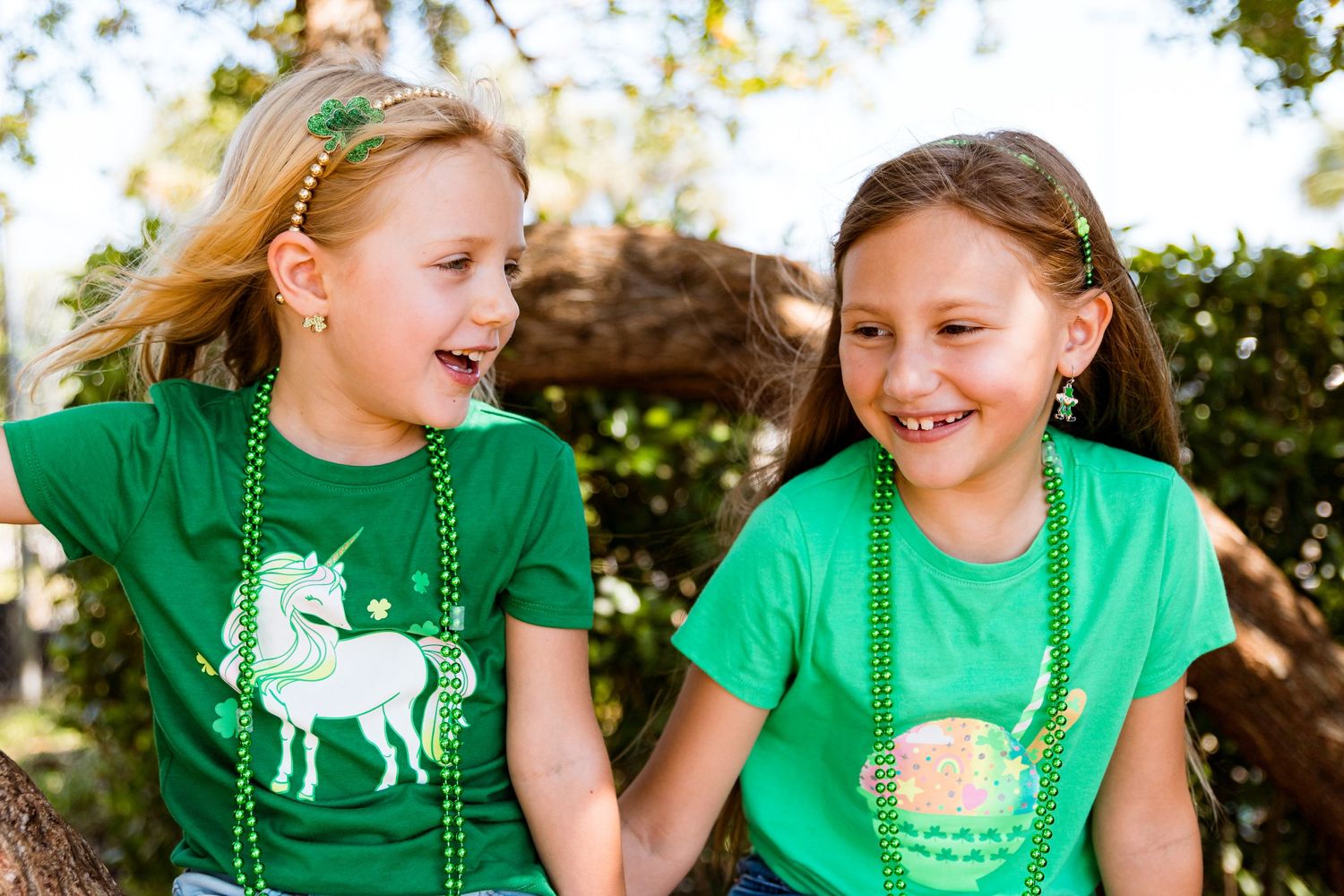 Children in green unicorn and rainbow shirts sharing a joyful moment outdoors.