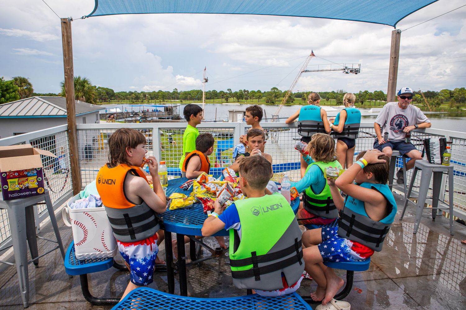 Group of people in life jackets sitting on a dock overlooking a lake on a sunny day.