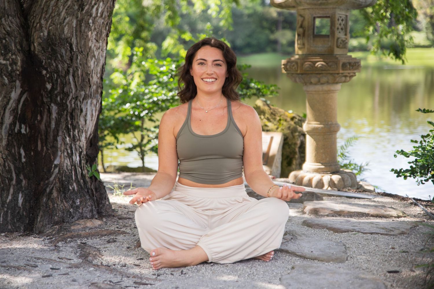 Someone practices meditation in a lotus pose by a serene pond with a stone lantern in the background.