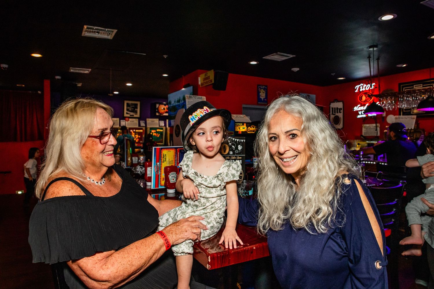 Three women, one older and two younger, posing together in a bar or restaurant setting.