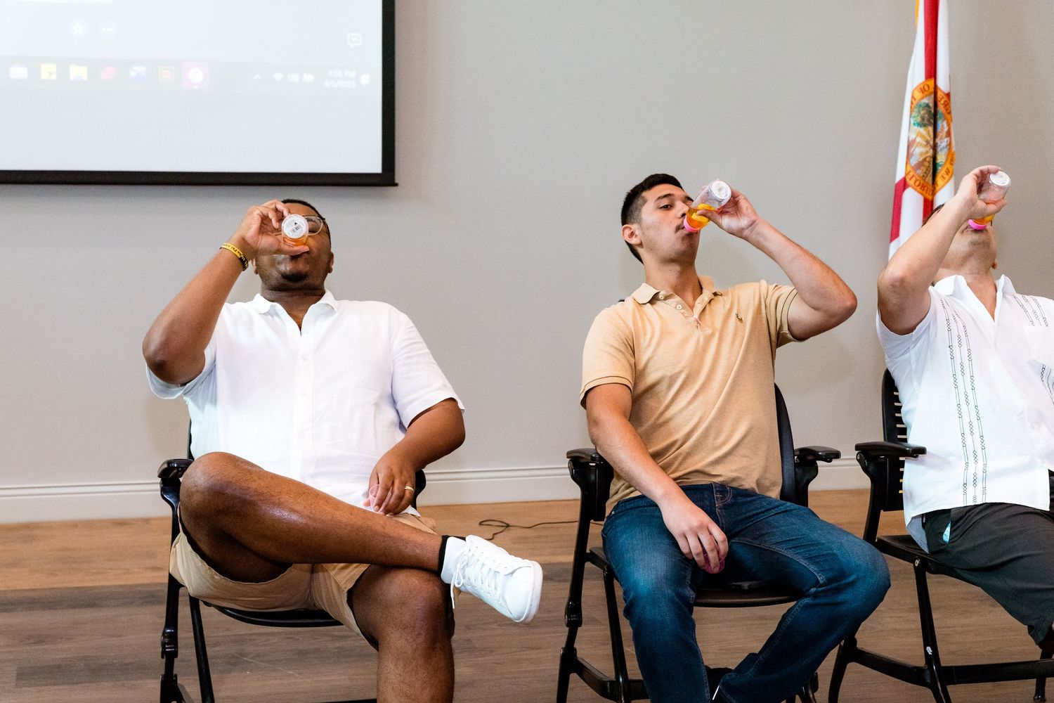 Three guests enjoying drinks while sitting in chairs at an indoor event.