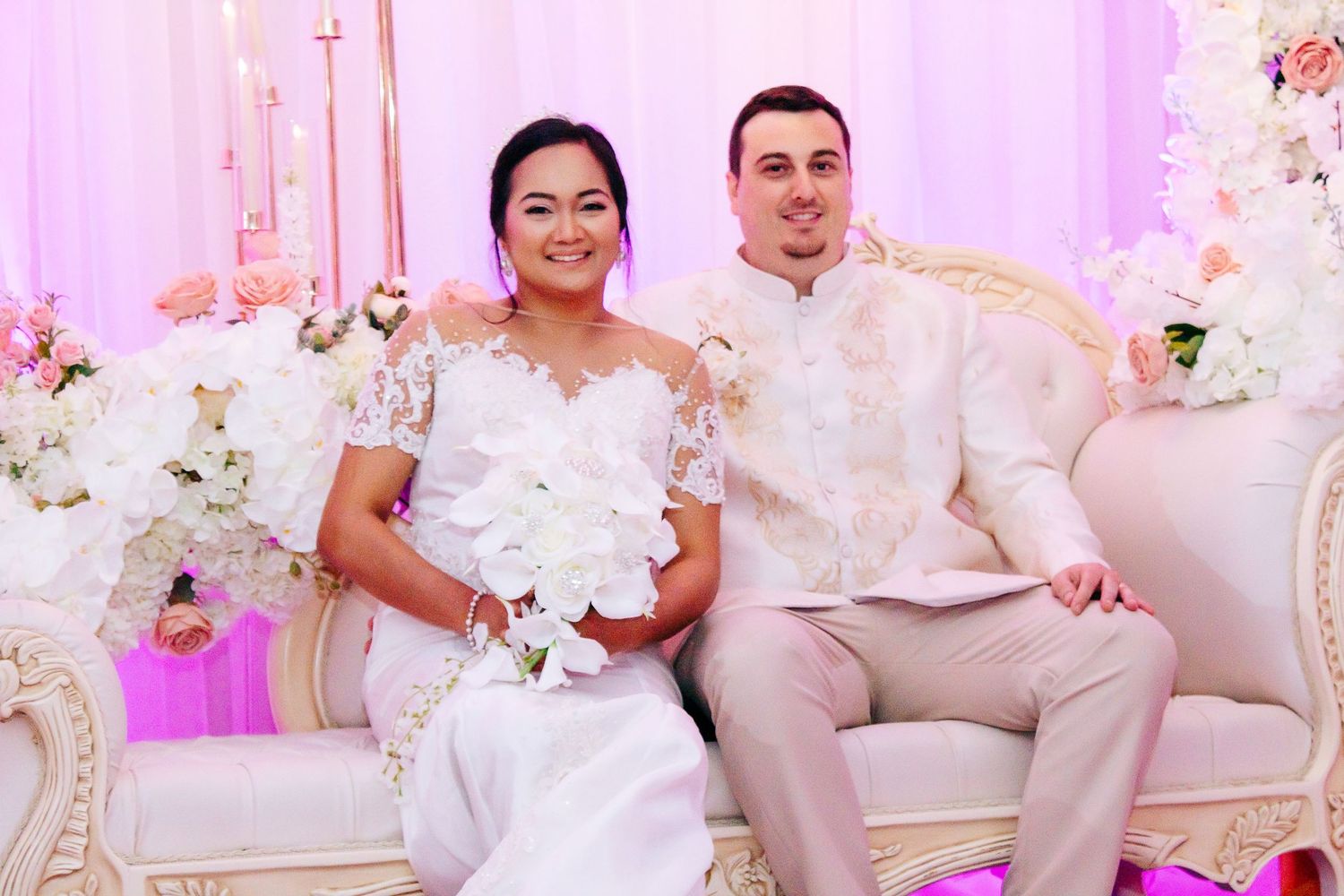 Wedding reception venue decorated in soft pink lighting with white floral centerpieces and elegant decor.