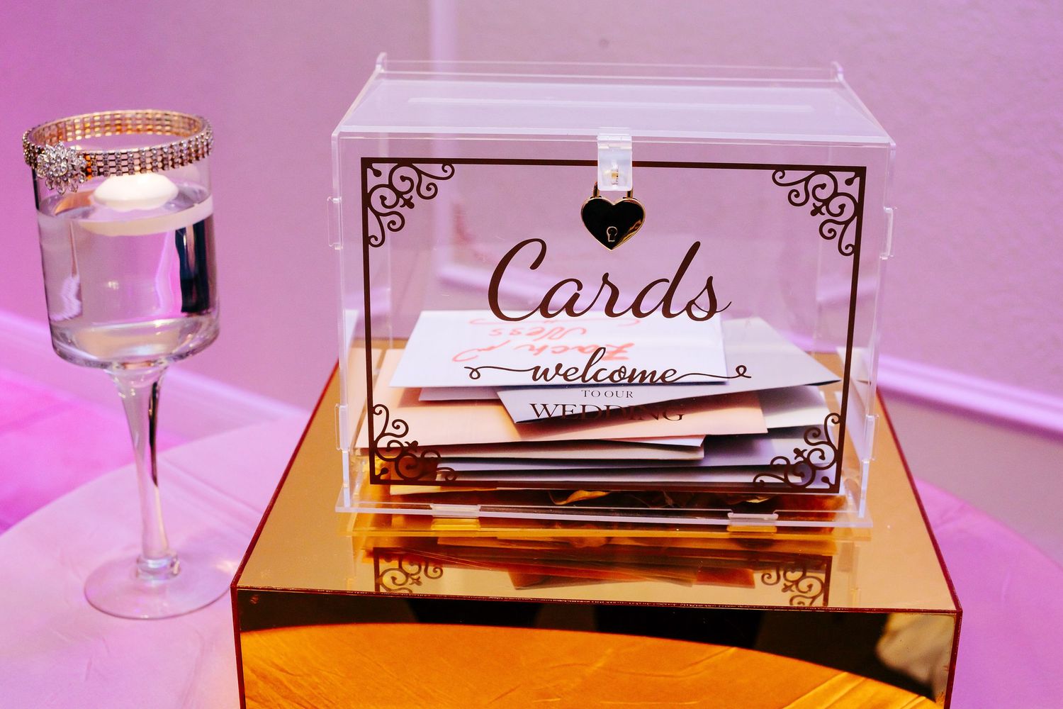 Elegant reception table details with cards and place settings under pink ambient lighting.