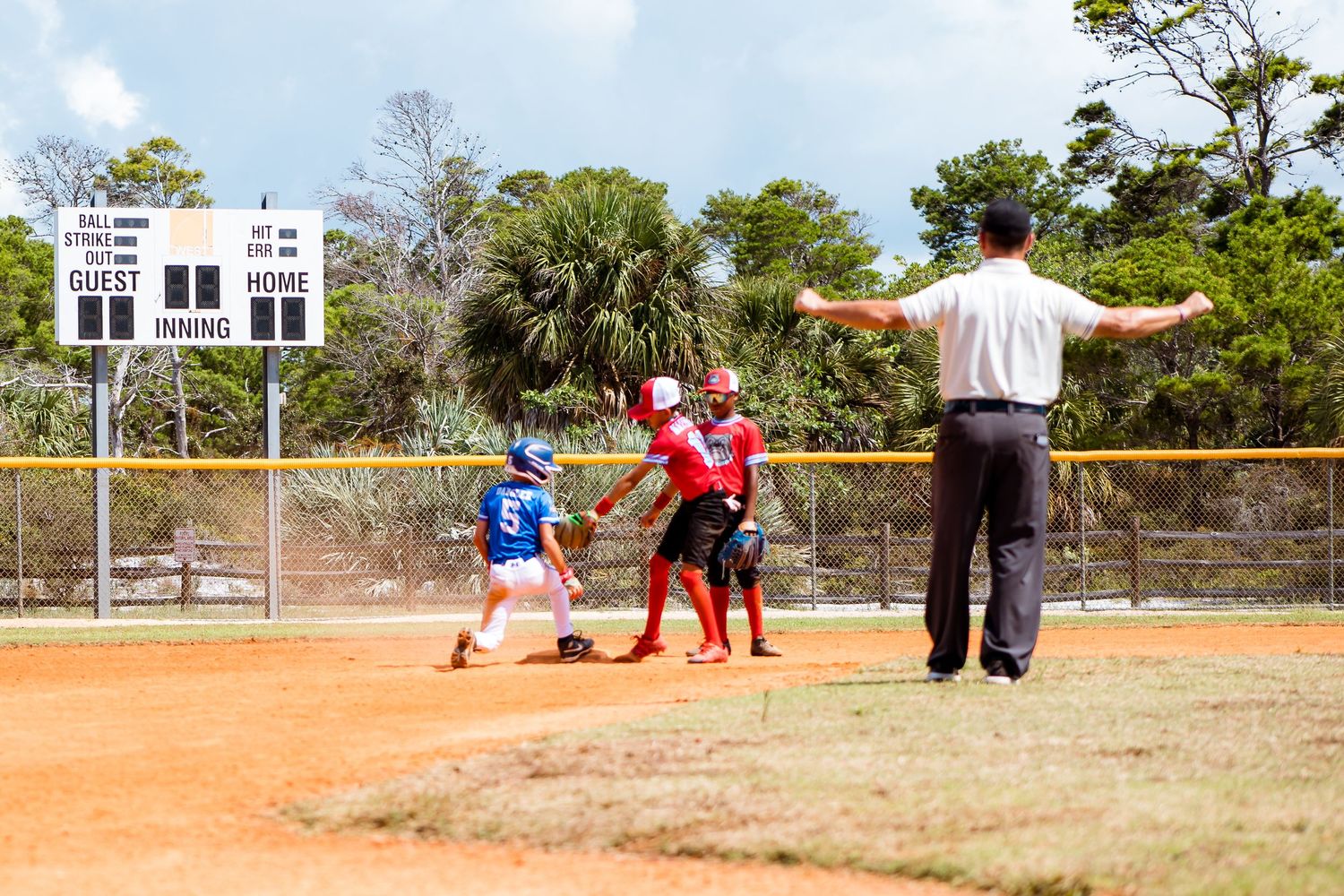 Baseball umpire makes call at home plate during youth game on dirt field.