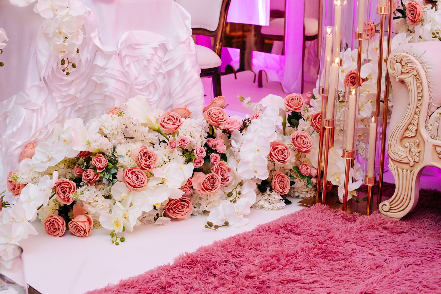 Pink and white roses cascading along a luxury seating area with pink carpet and ambient lighting.