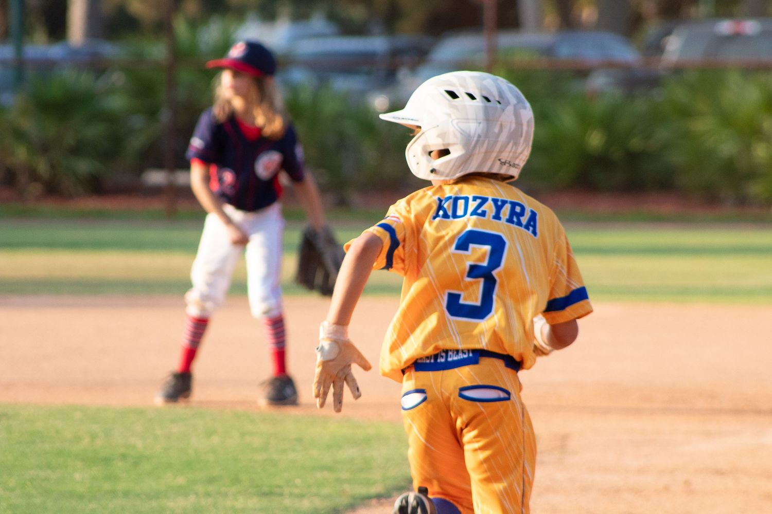 Baseball player wearing orange uniform with number 3 stands ready on base during game.