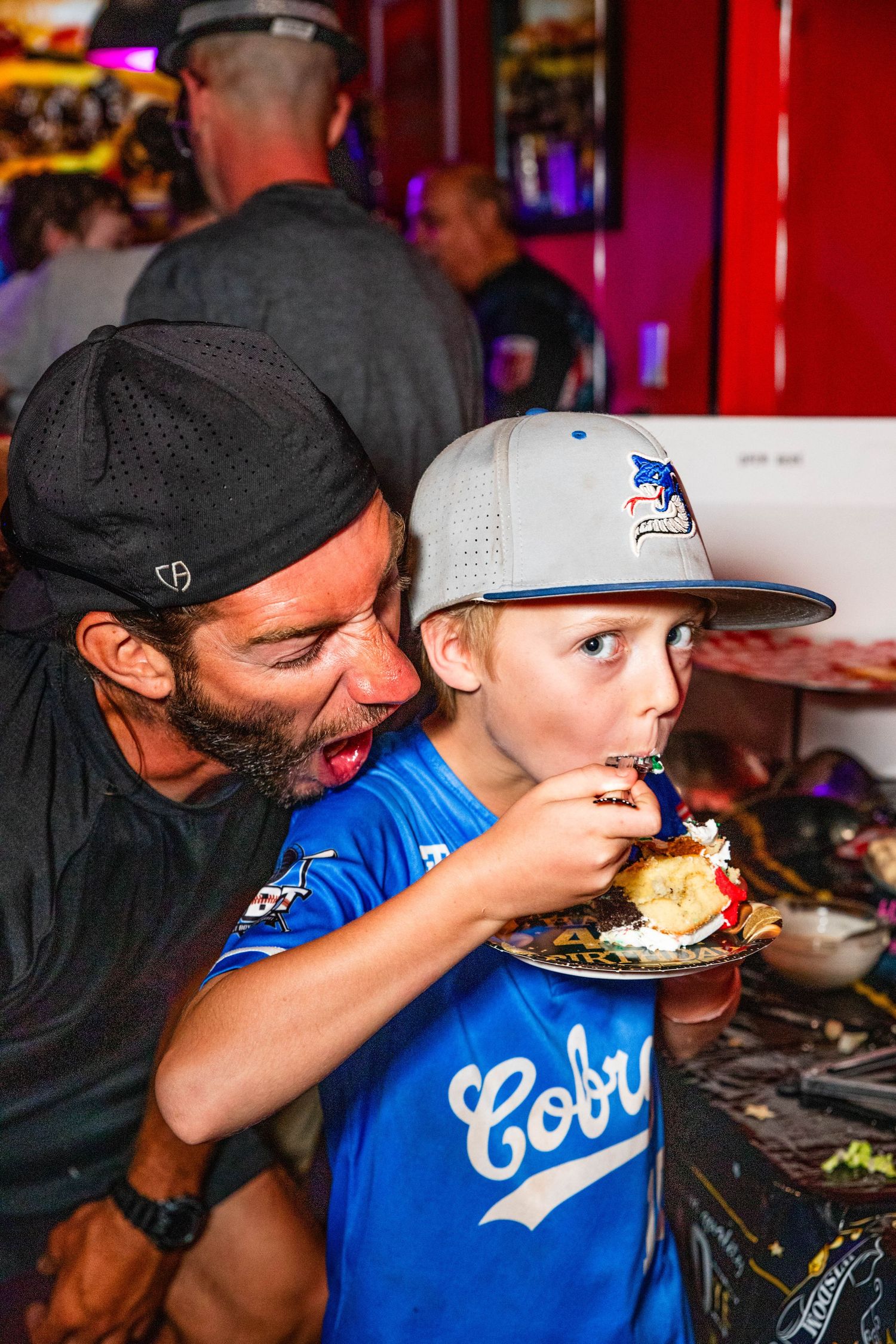 A man and a young child eating food together at a bar with arcade games.