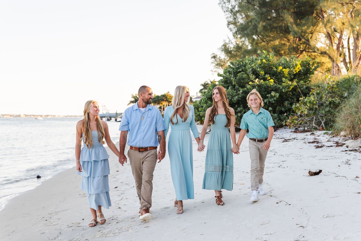 Group walking along white sandy beach at sunset wearing coordinated blue and mint colored outfits.