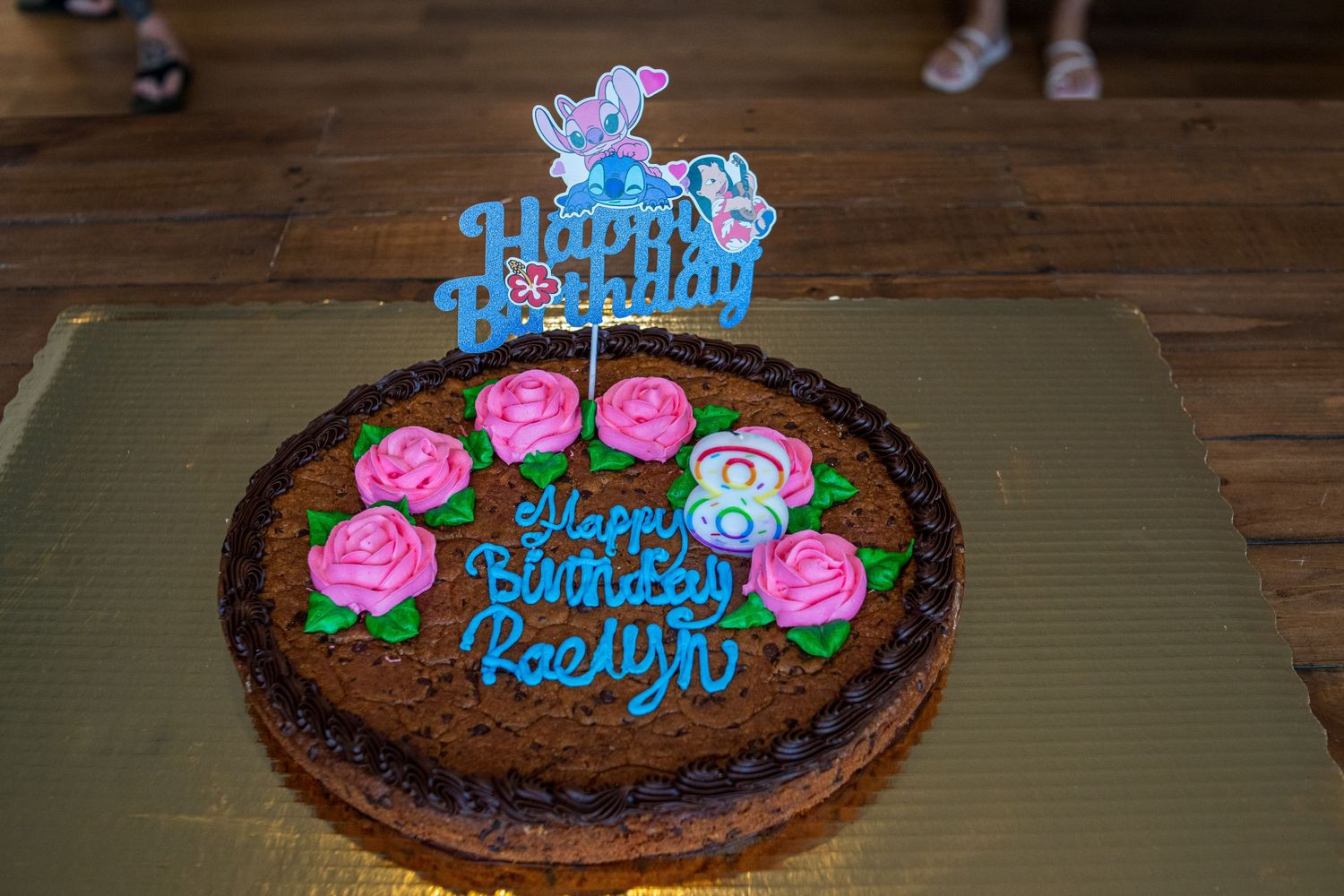 Decorated chocolate birthday cake with pink and blue frosting roses and writing on a dark wooden table.