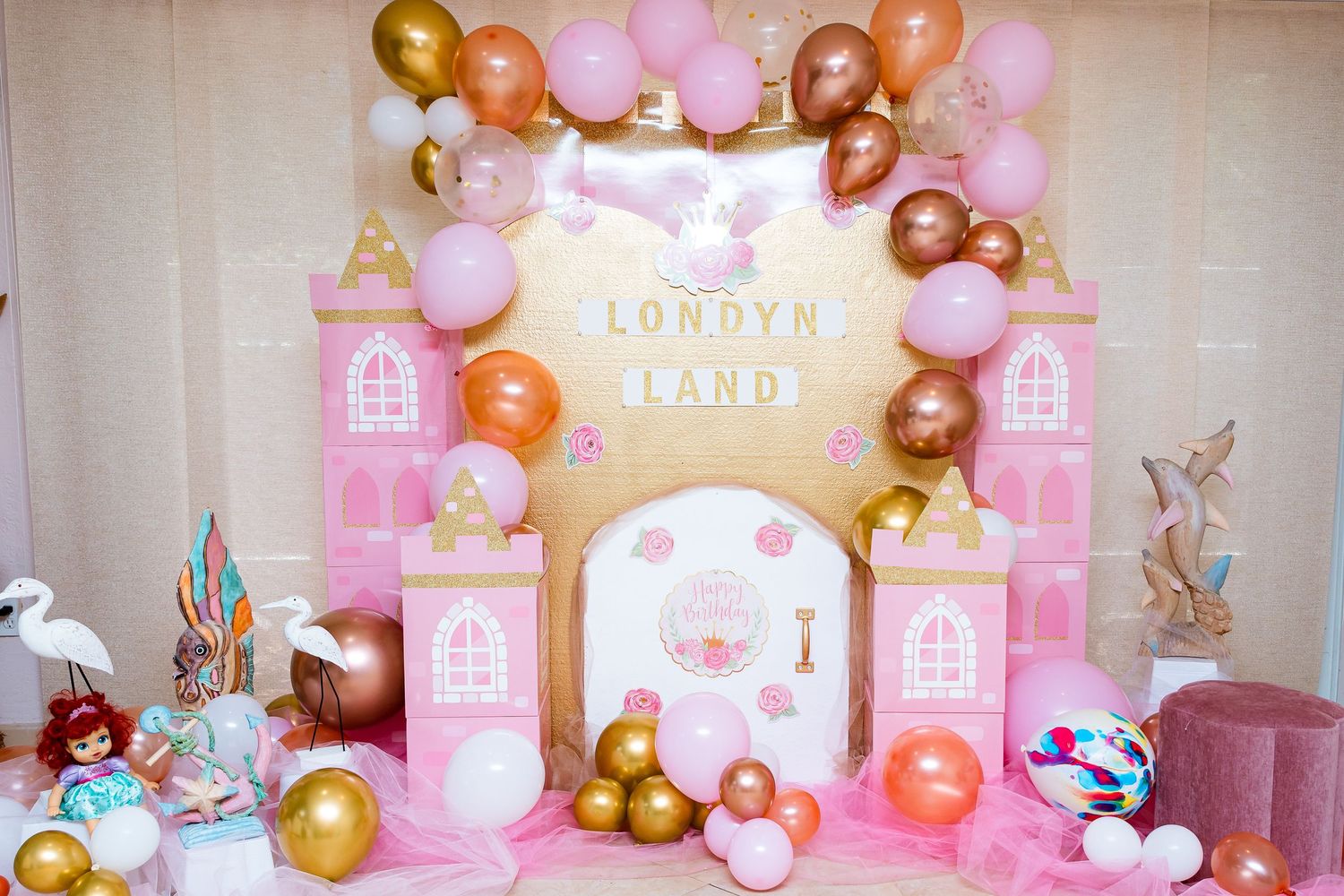 Pink castle backdrop with gold and pink balloon arch for a birthday party featuring whimsical tea party decorations.