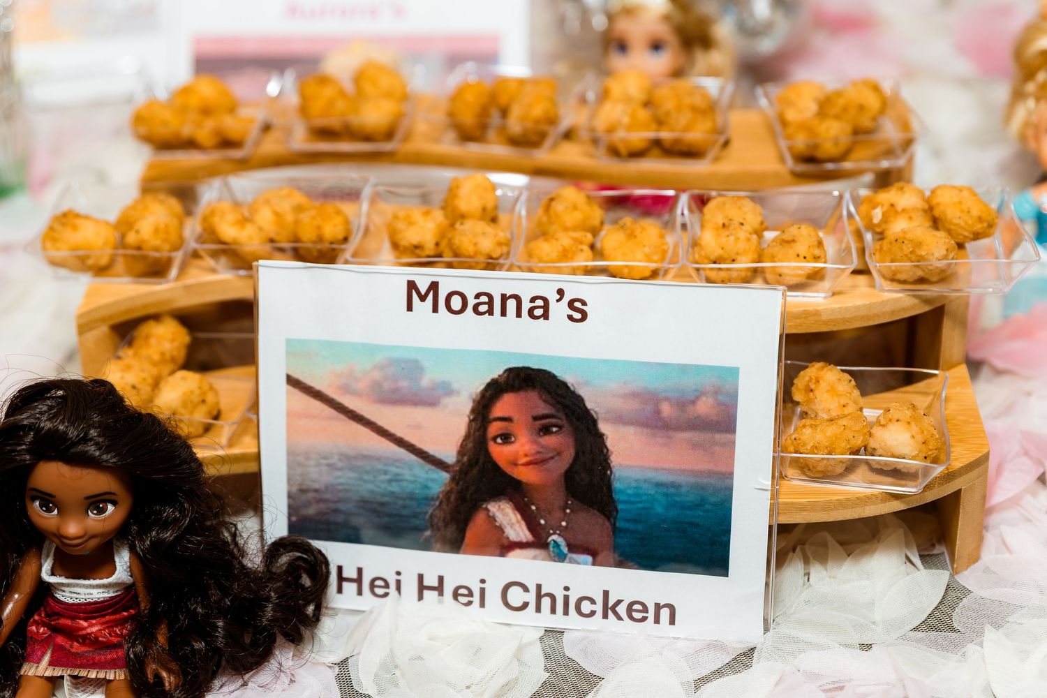 Orange Hei Hei chicken appetizers displayed on wooden platters at a Moana themed party with character decor.
