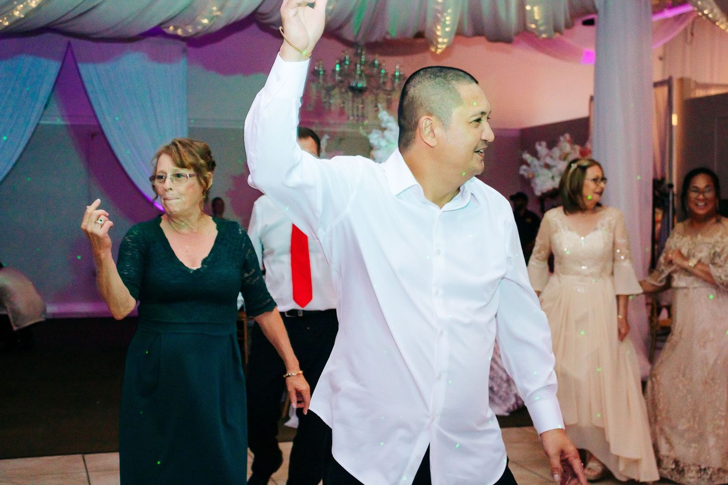 Party guests dancing and celebrating on the dance floor with elegant draping in the background.