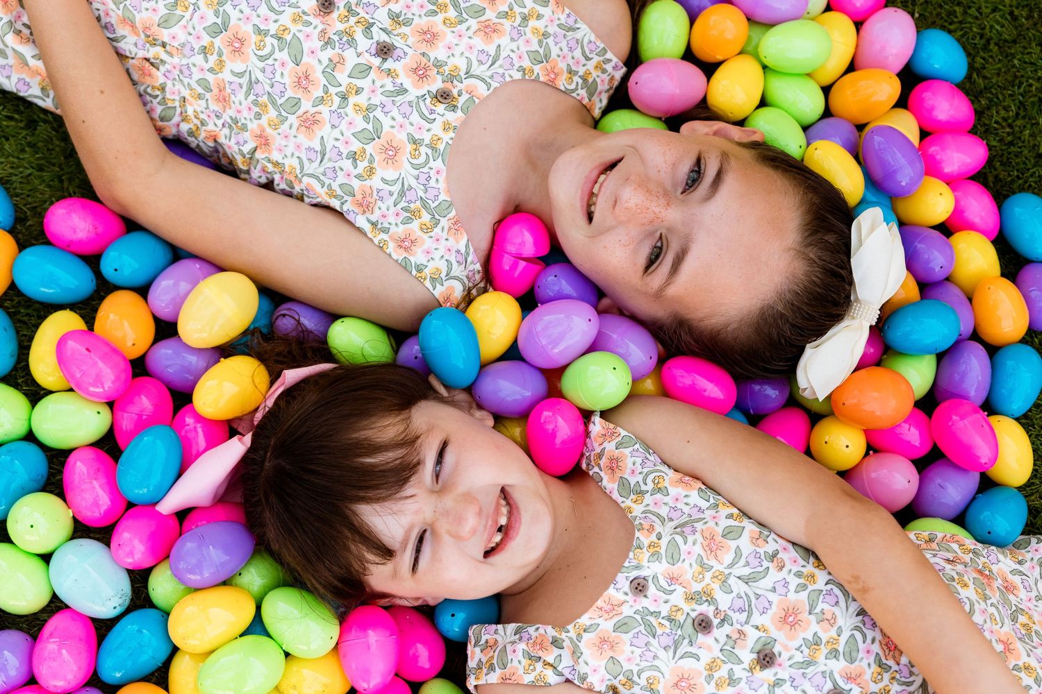 Two people in matching floral outfits lying down surrounded by bright multicolored plastic Easter eggs.