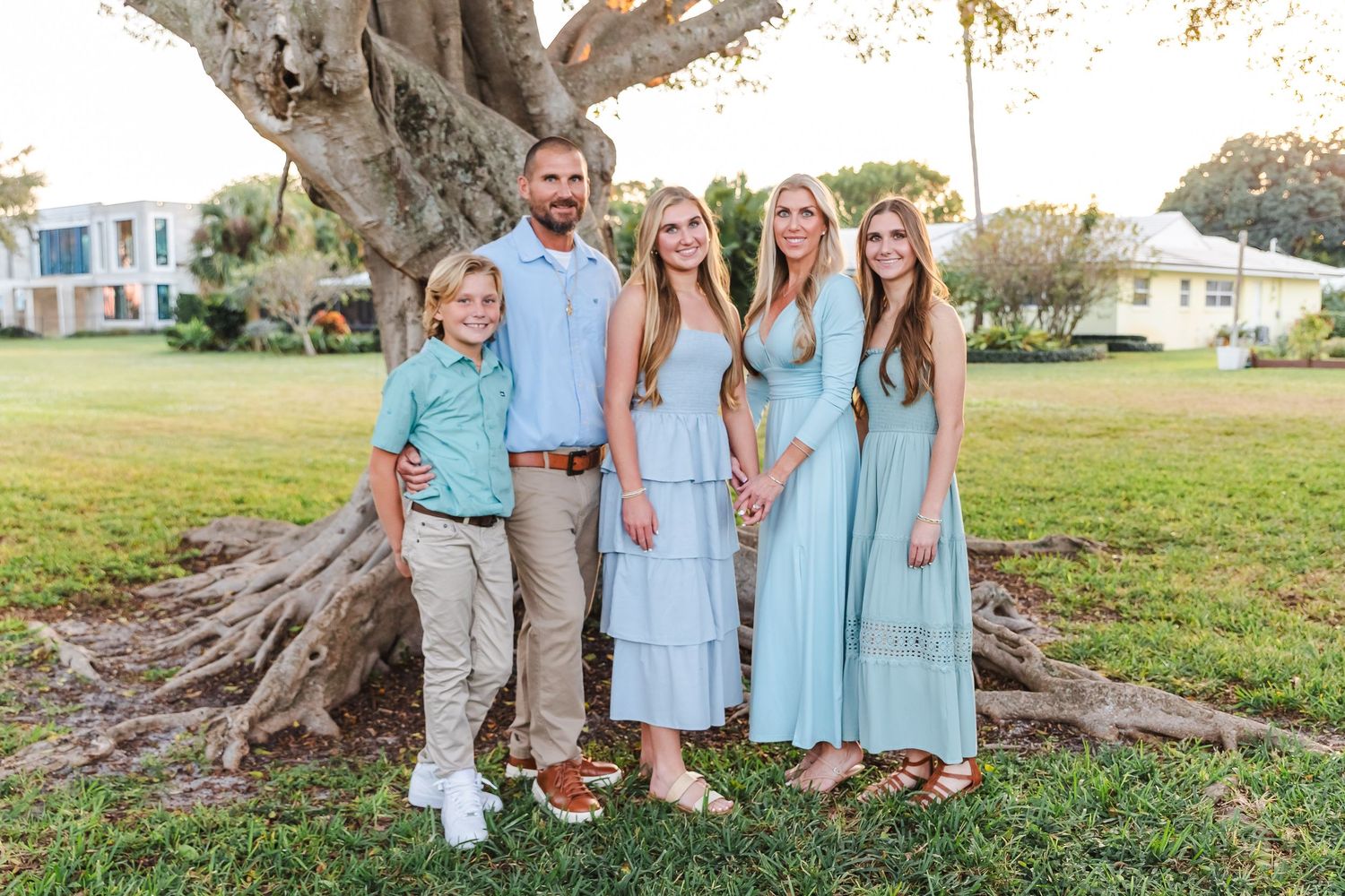 Family portrait in coordinating blue outfits posed in front of a large tree.