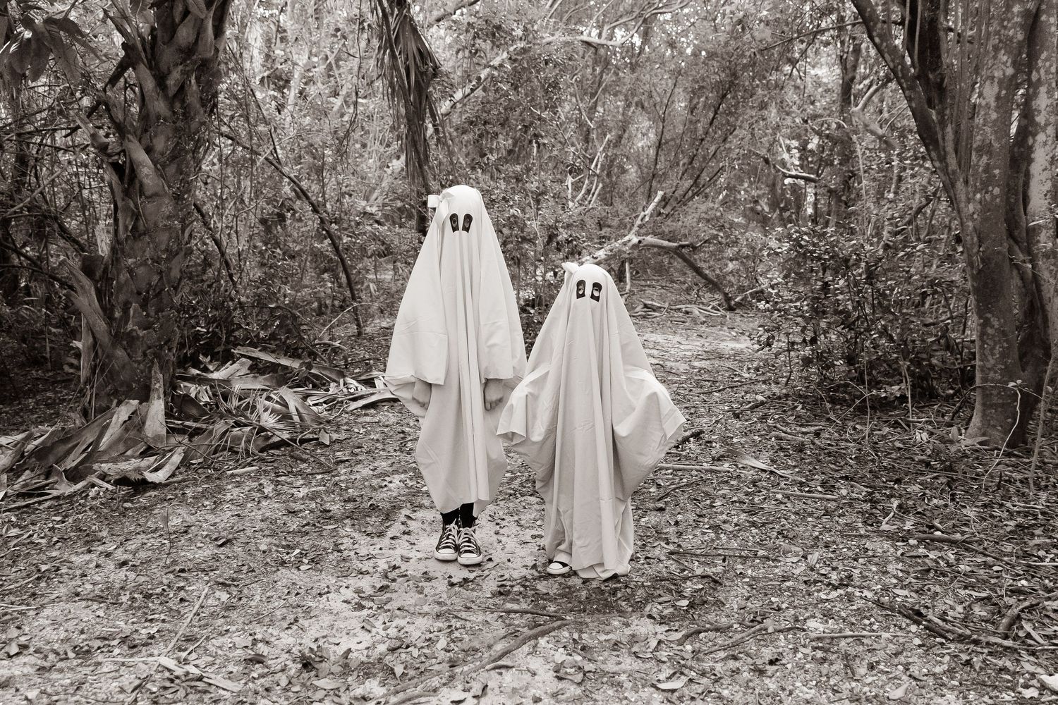 Seven black and white photos show ghost costumes in a spooky forest setting creating an eerie Halloween atmosphere.