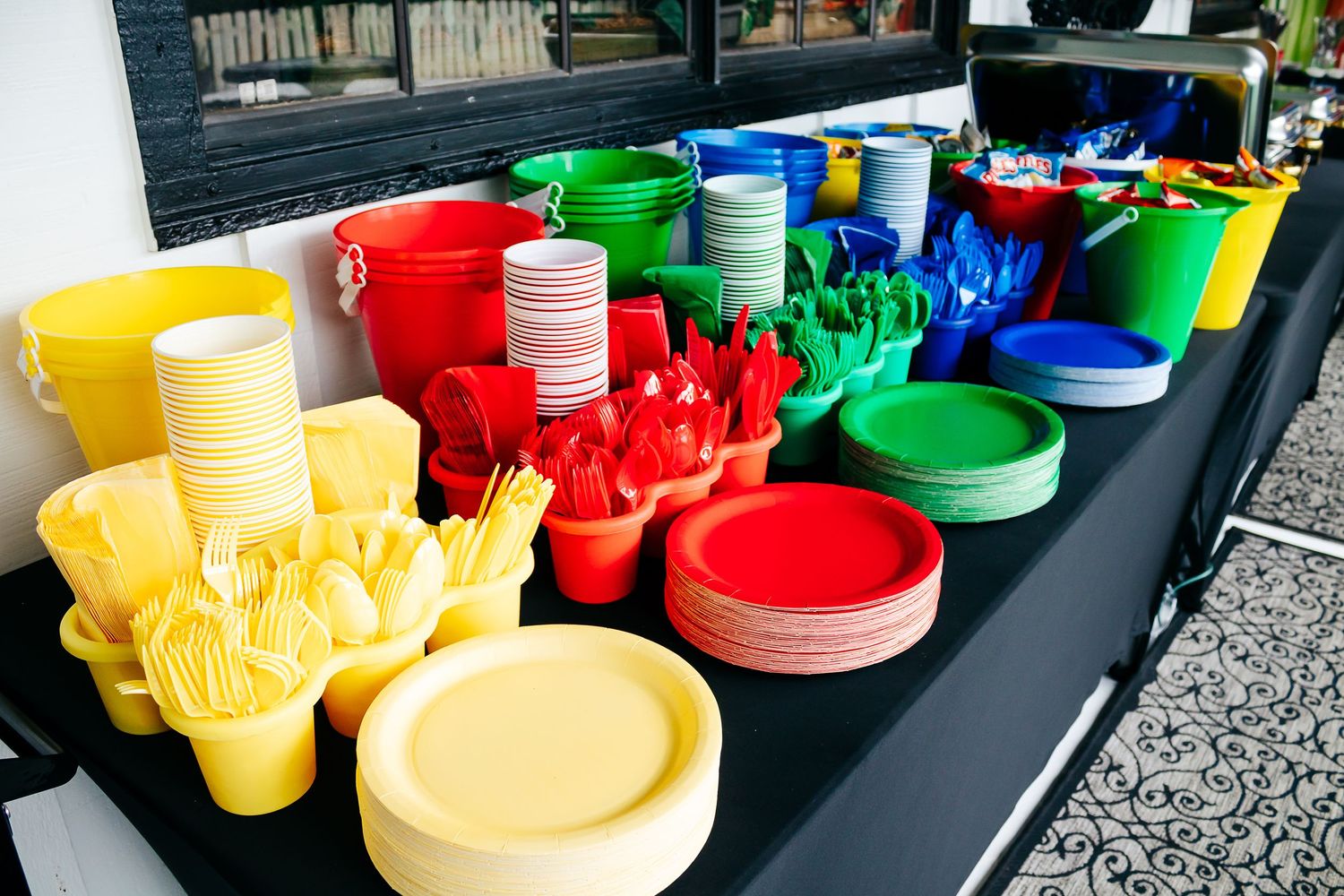 Colorful plastic plates and cups arranged on a black table at what appears to be an outdoor event setup.