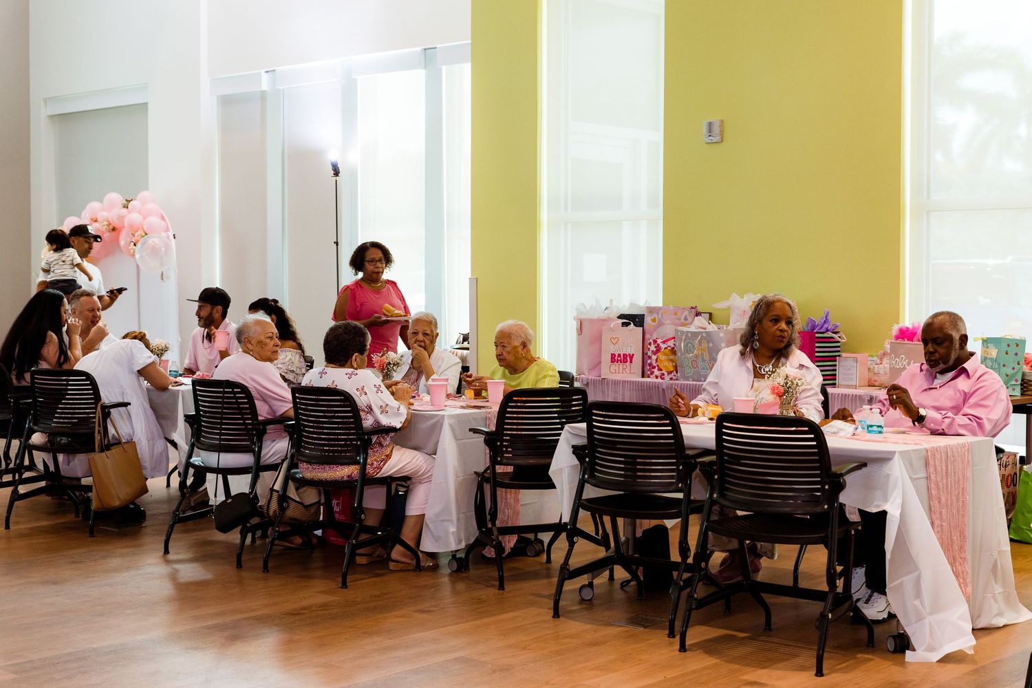 People seated at tables in a bright room with yellow walls for a daytime gathering.