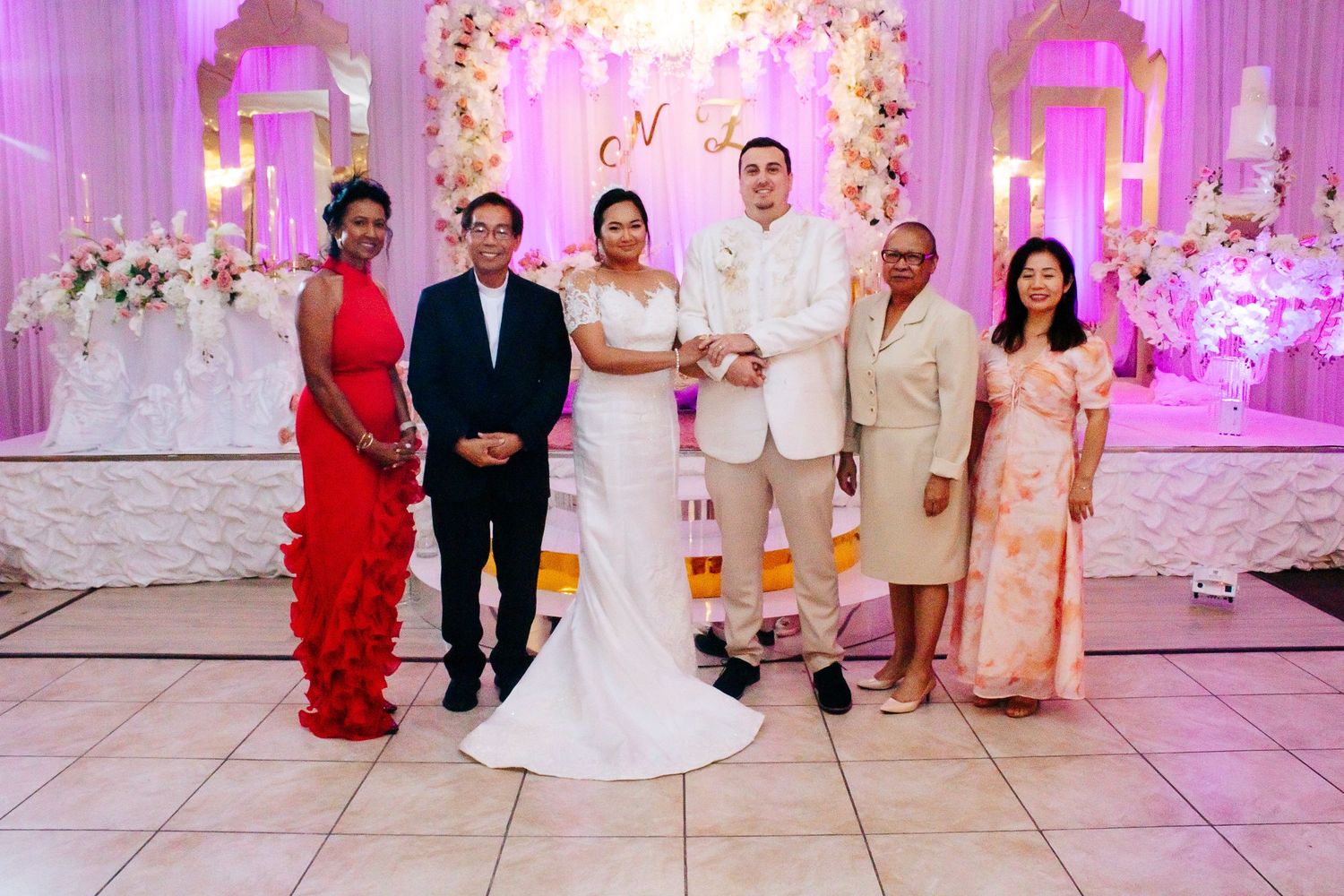 An elegant wedding reception venue decorated with pink lighting and floral archways.