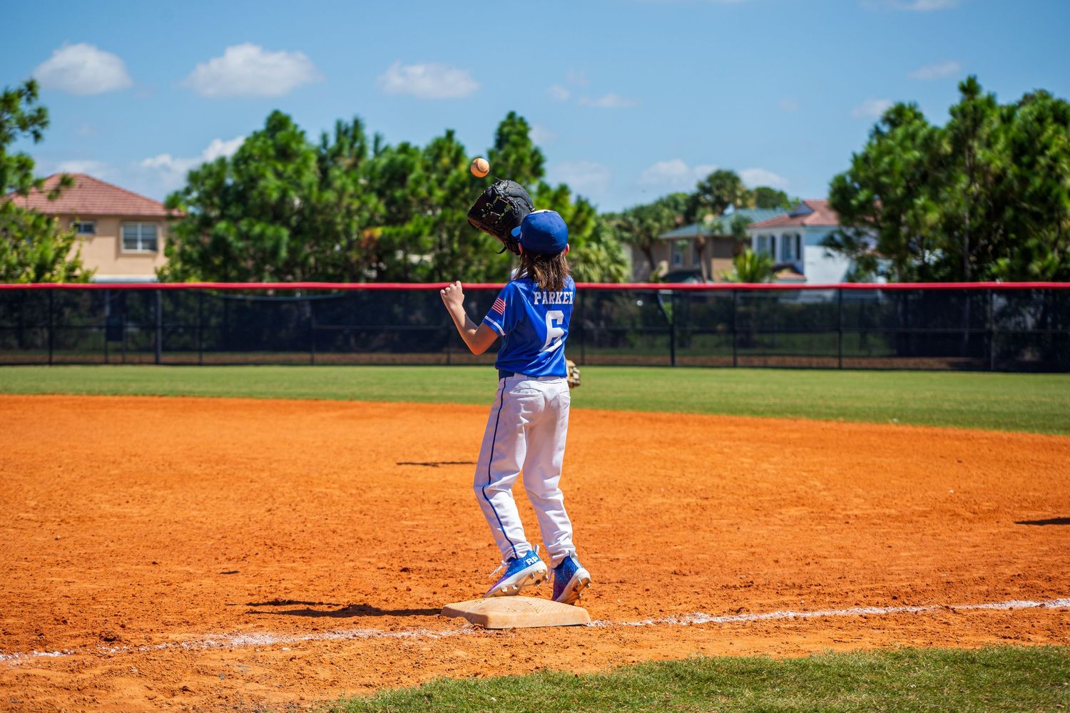 Baseball player in blue uniform stands on dirt infield during sunny afternoon game.