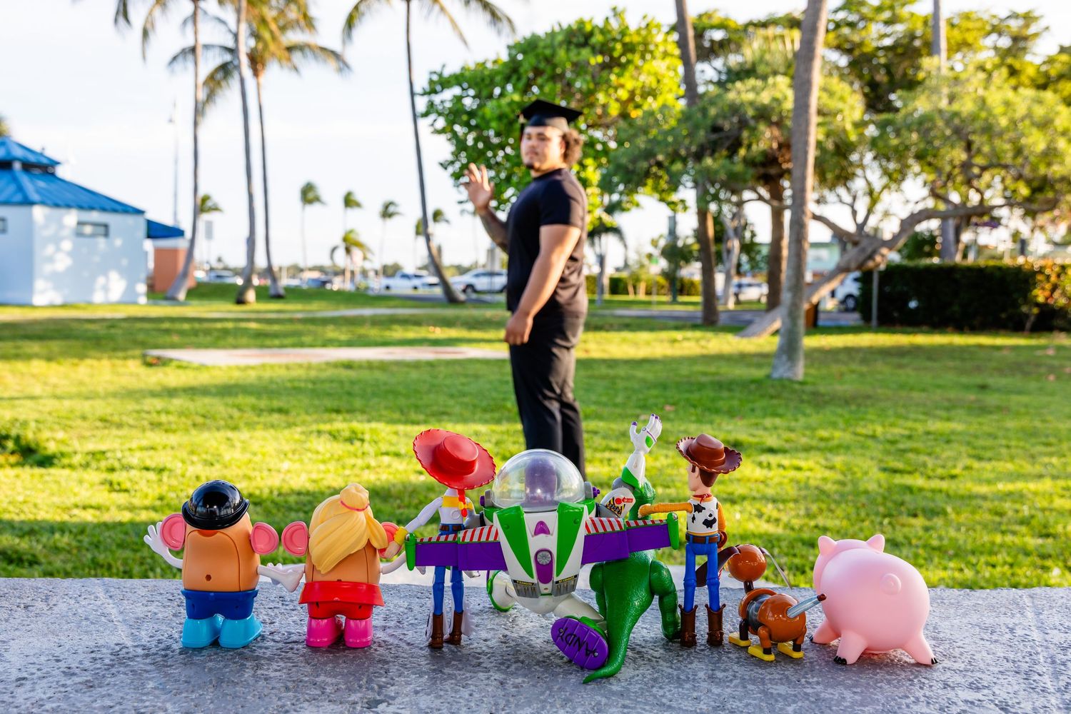 Man standing outdoors with Toy Story character figurines including Buzz Lightyear, Woody, and Hamm on pavement.
