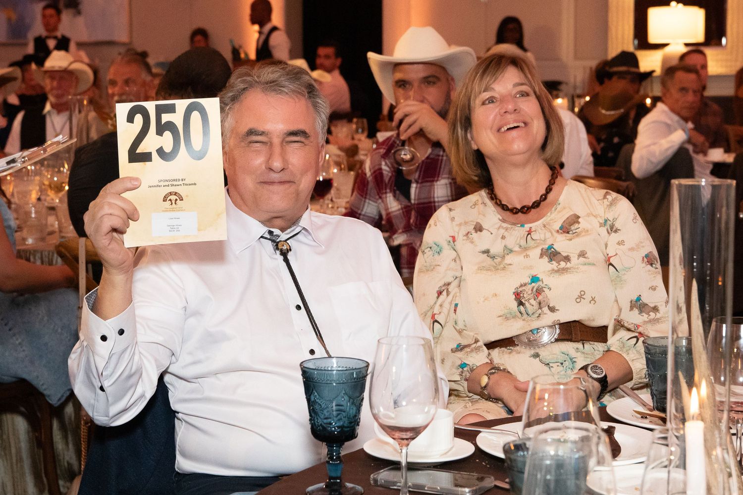 Couple at formal dinner event holding up auction paddle number 250.