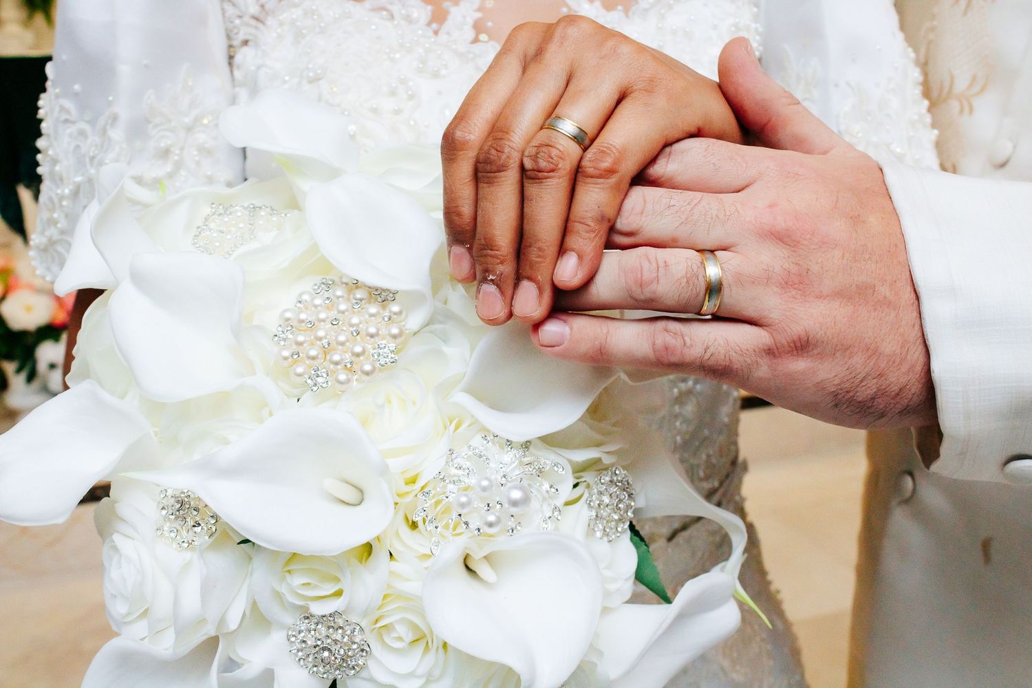 Close-up of couple's hands showing wedding rings against white floral bouquet.