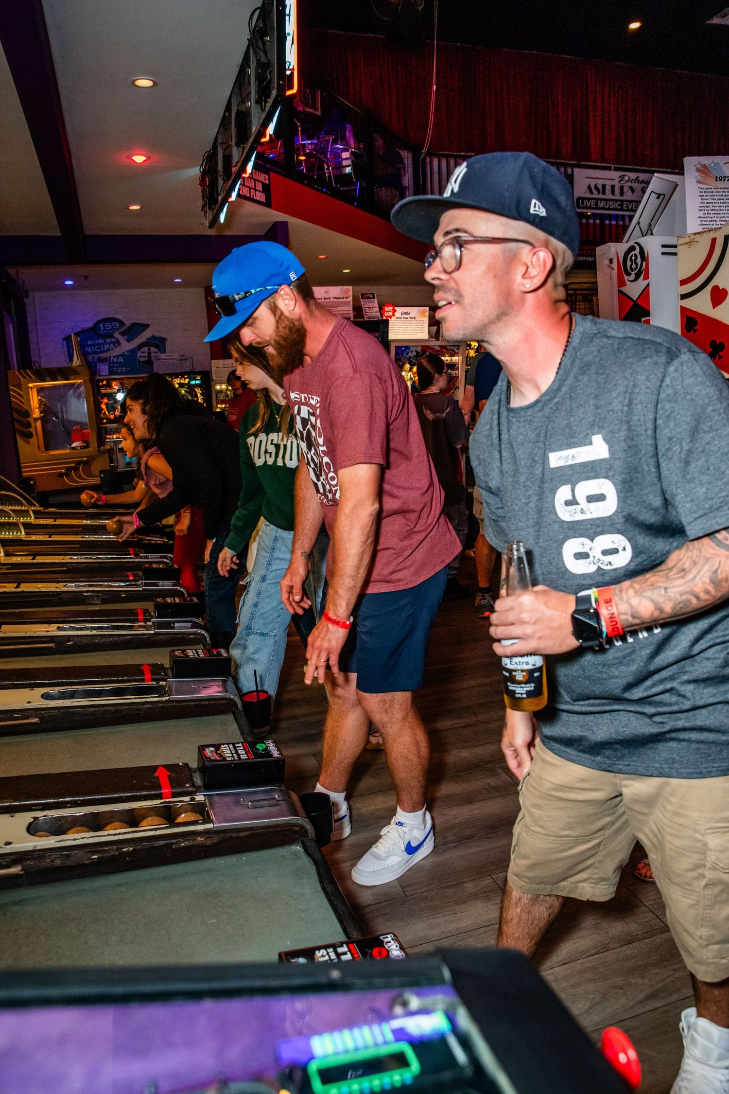 A group of people are gathered around and playing a pinball machine in an arcade environment.
