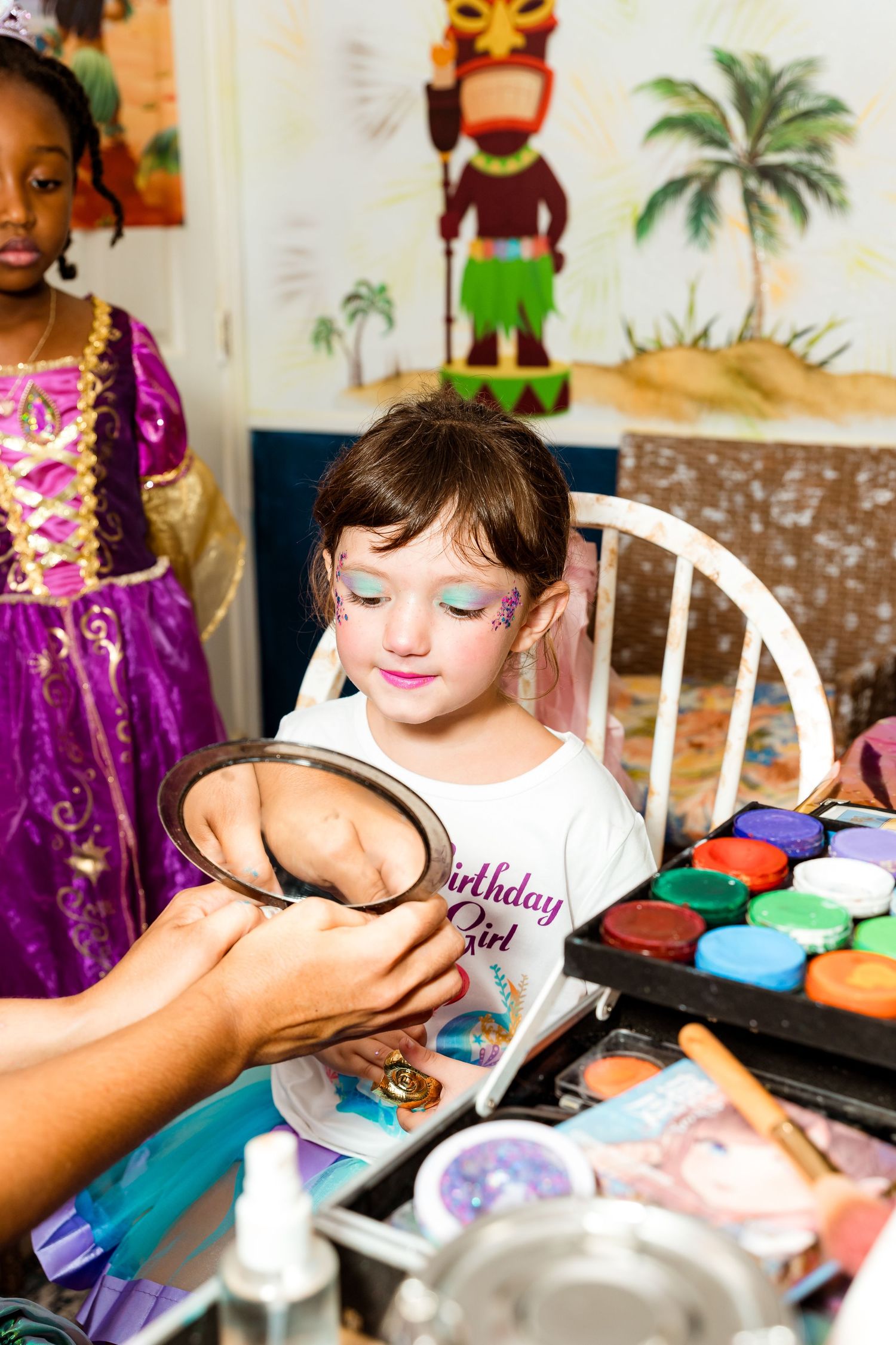 Child getting face painted at a princess-themed party with colorful makeup palette.
