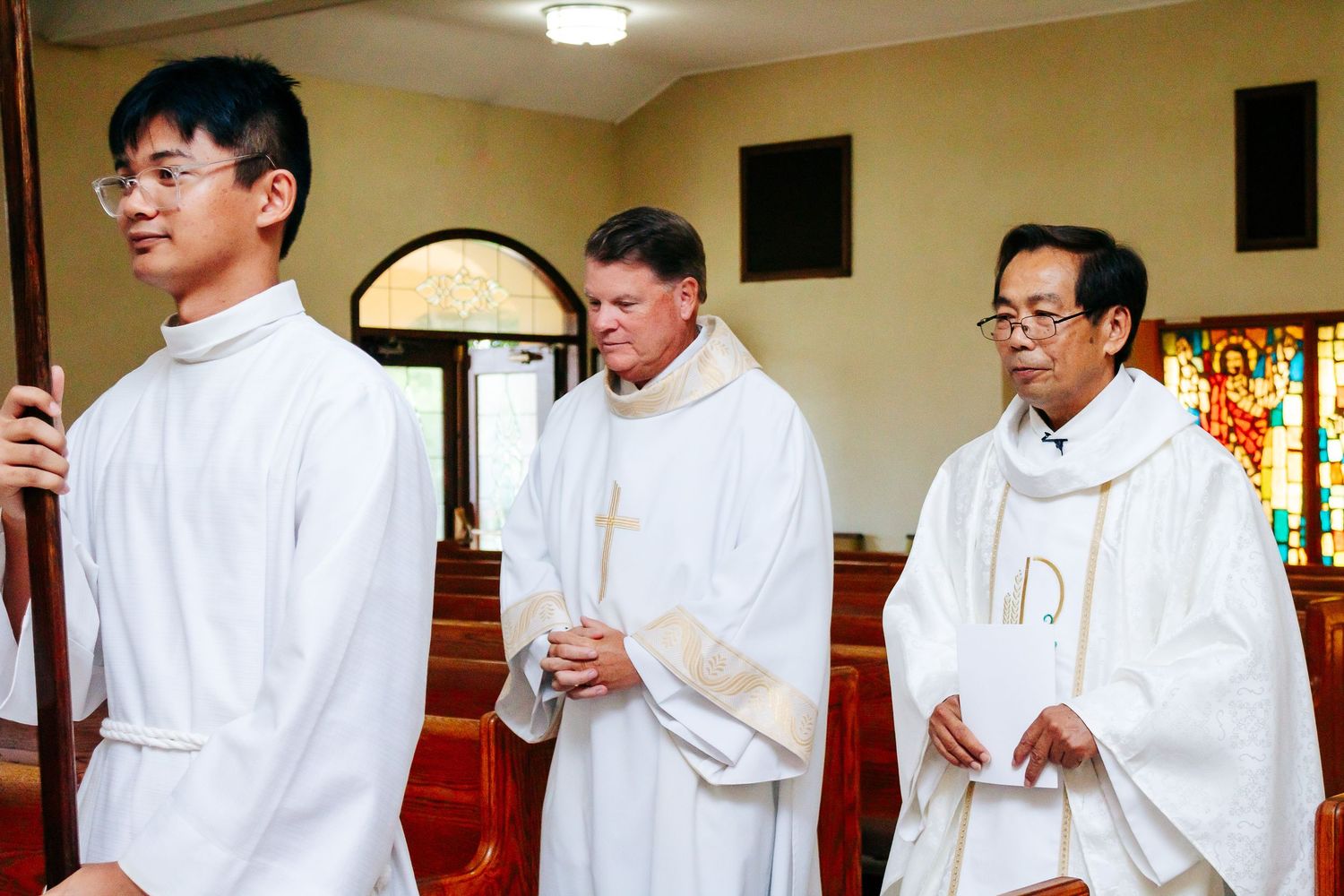 Row of groomsmen in white formal attire standing together inside a church sanctuary.