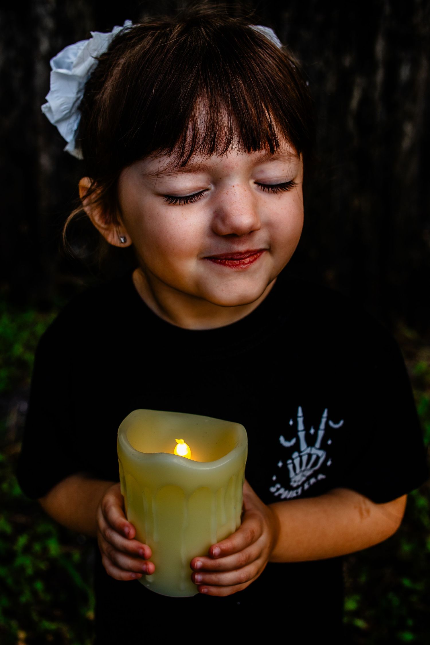 Child holding glowing candle while wearing Halloween themed shirt.