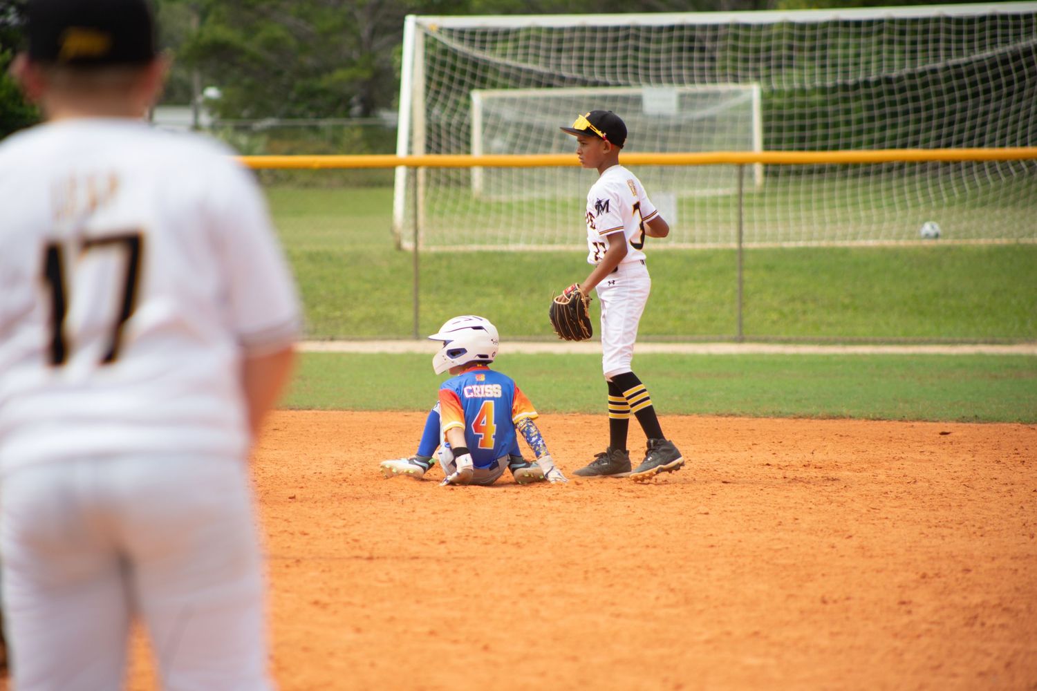 A baseball play on a dirt infield with a runner sliding into base as a defensive player stands nearby.
