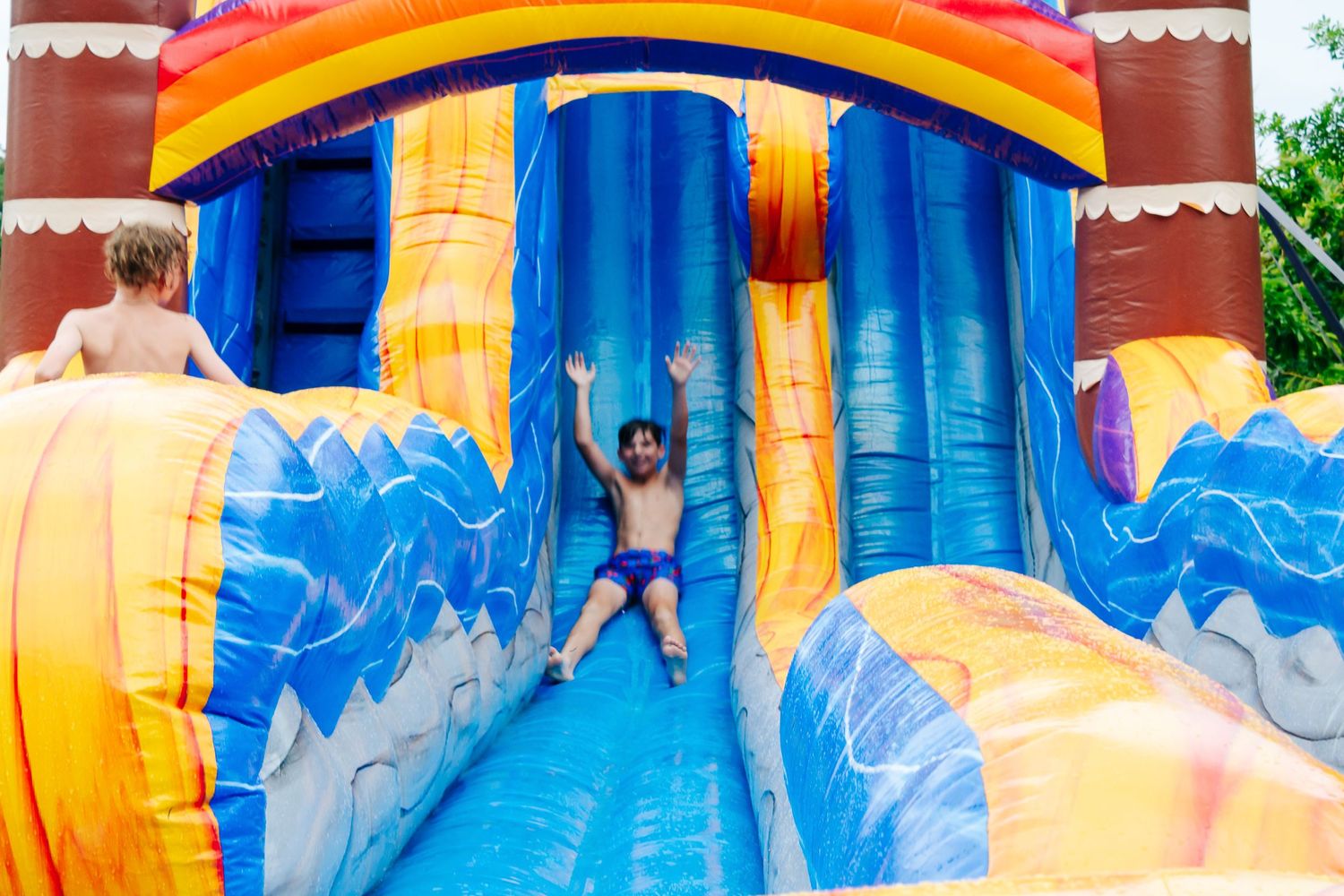Child sliding down a vibrant inflatable water slide at an outdoor party.