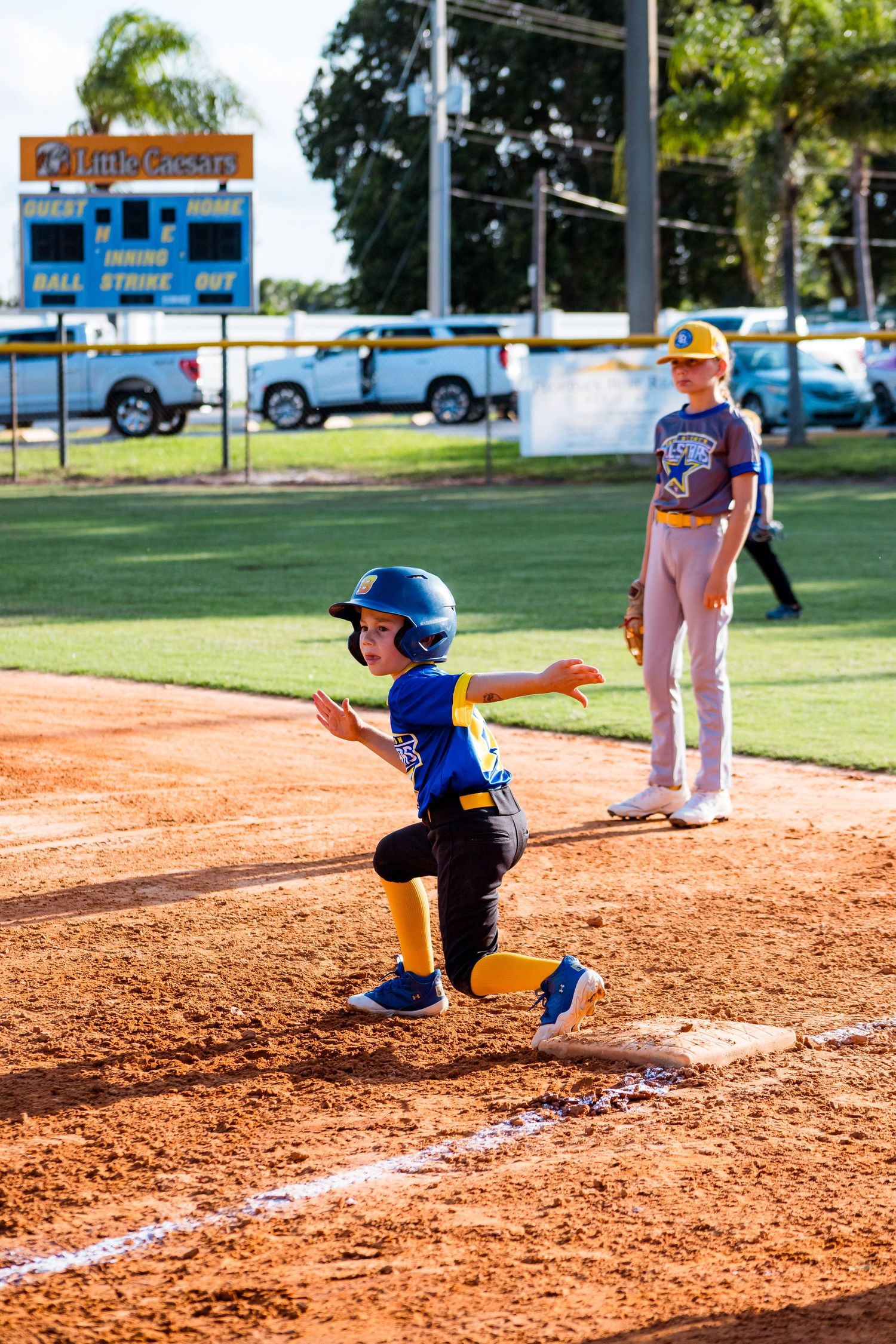 Young baseball player in blue uniform practicing batting stance at home plate on dirt infield during youth game.