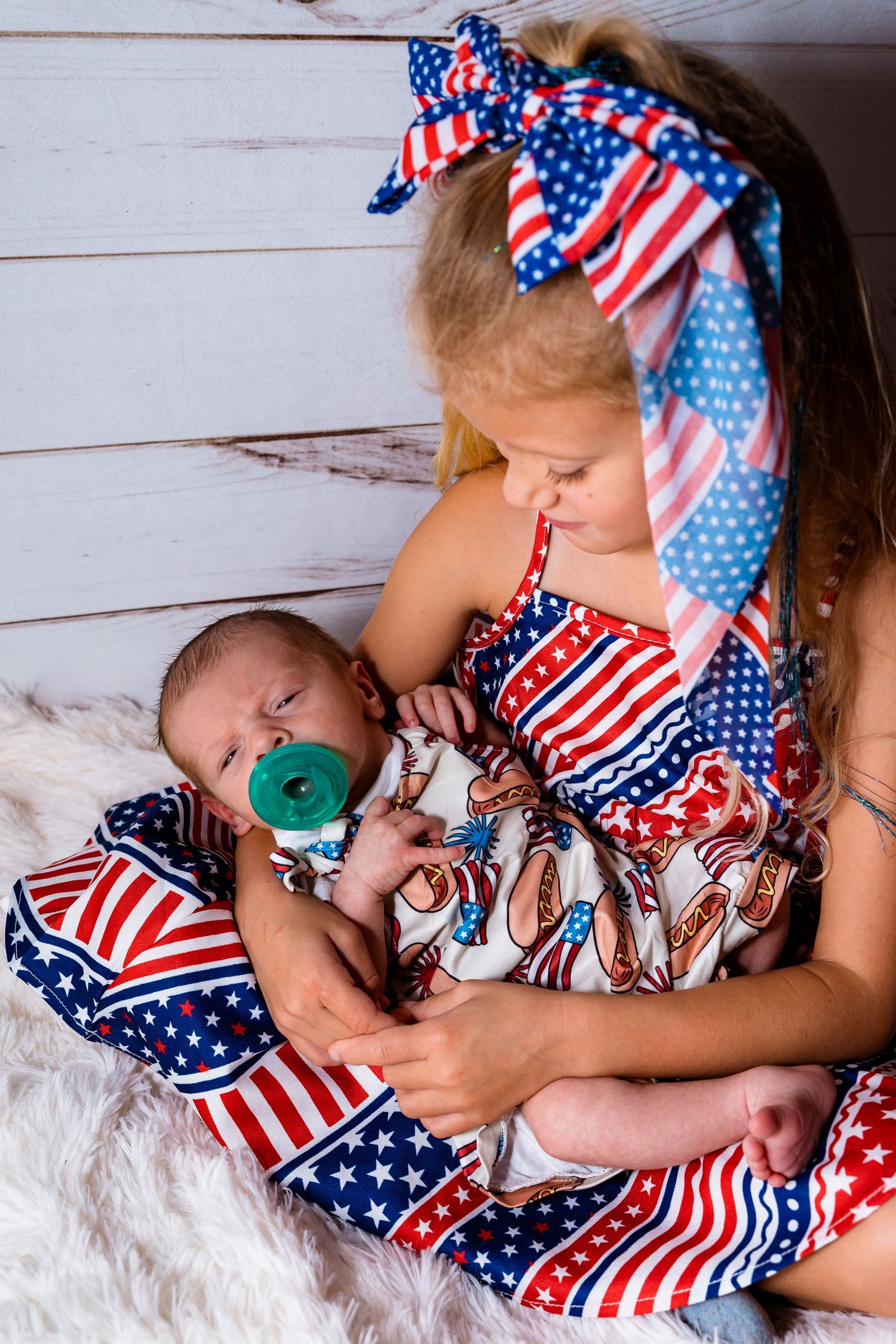 Two children in patriotic American flag print outfits sitting together on white fur.