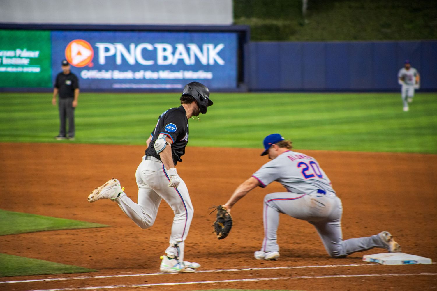 Baseball player slides into base during game at PNC Bank stadium while fielder attempts to make the play.