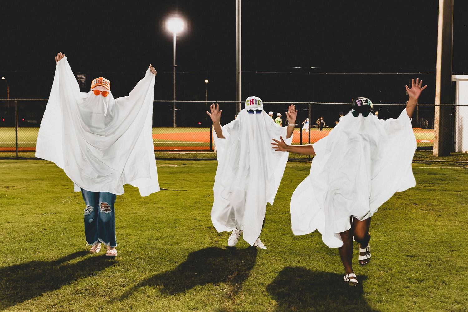 People wearing white ghost costumes pose playfully on a baseball field at night.