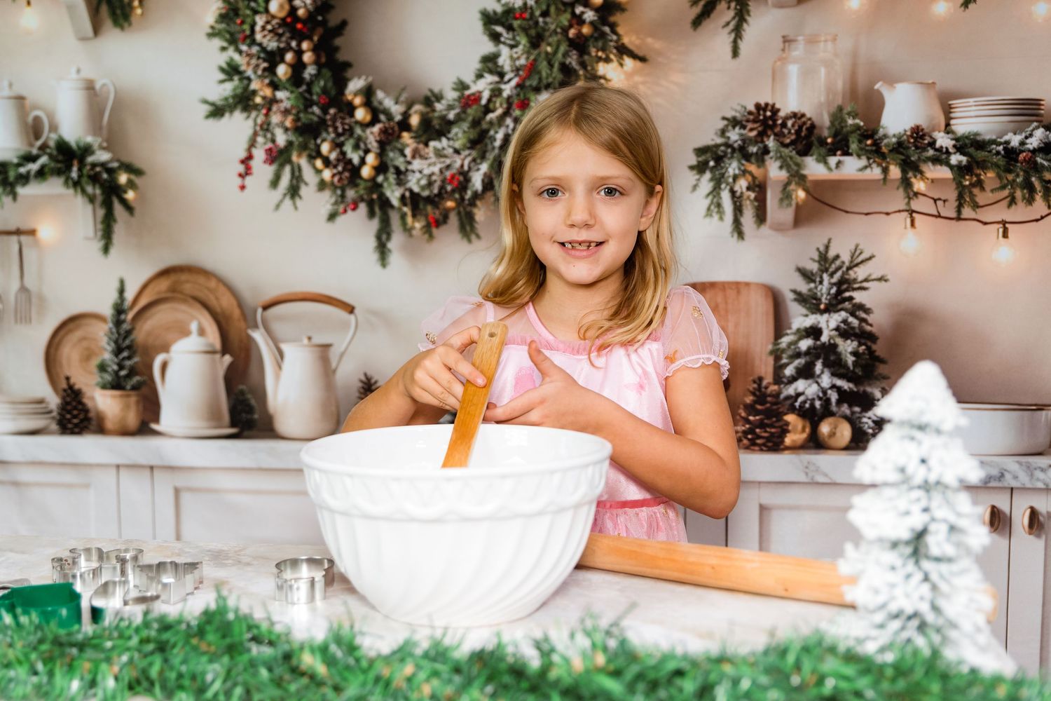 Holiday baking scene with child stirring ingredients in white mixing bowl near Christmas decorations.