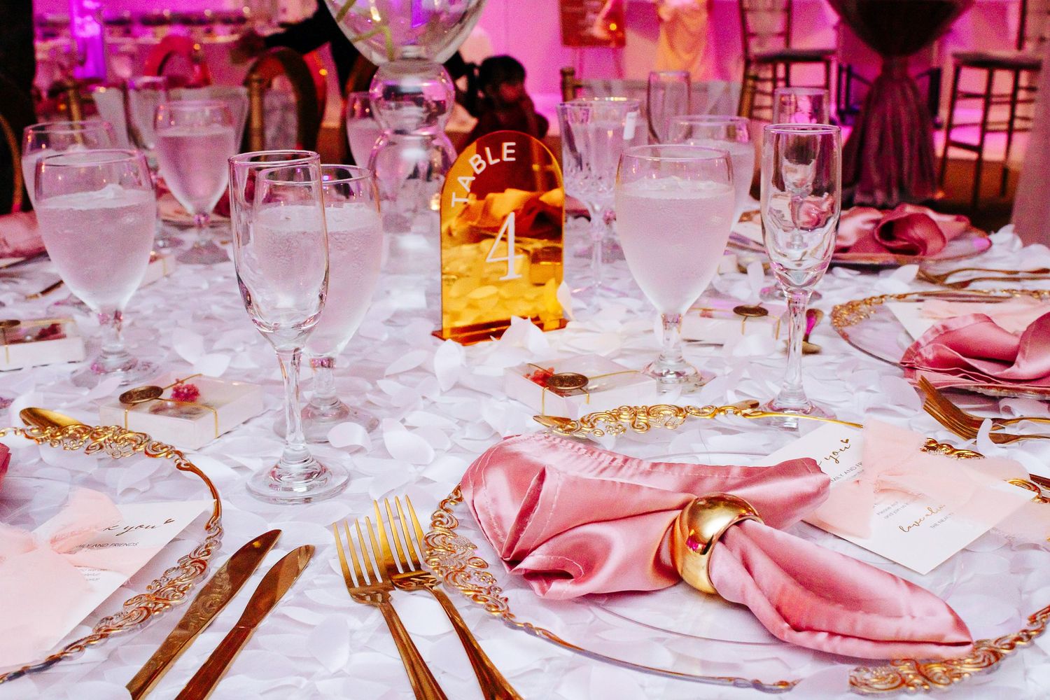 Formal table setting with pink napkins and glassware at wedding reception.