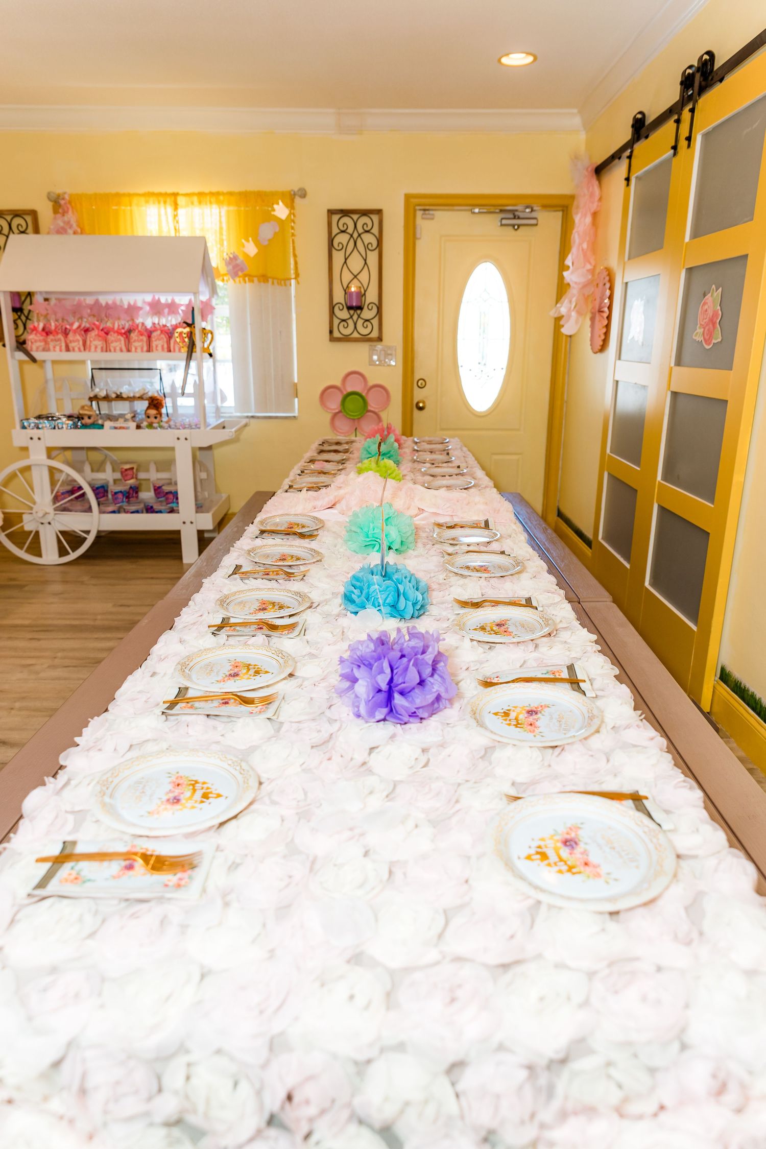 Long white decorated party table set up for a celebration with colorful accents and place settings.