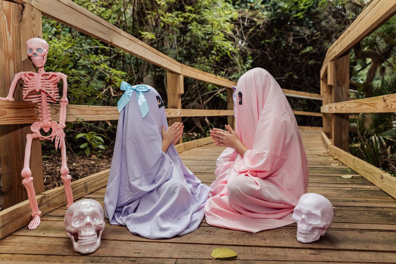 People in pink and white clothing sit together on a wooden deck surrounded by lush greenery.