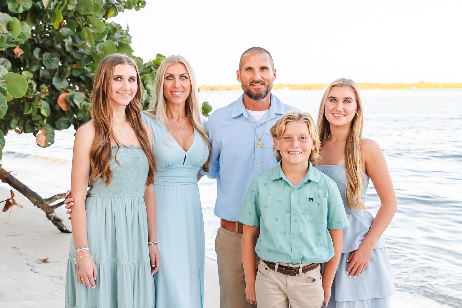 A group wearing coordinated mint green and white outfits poses together for beach family photos at sunset.