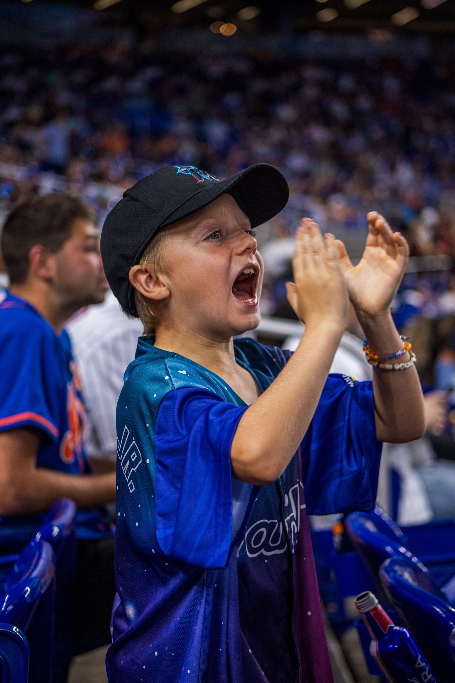 Young baseball fan in team jersey cheers excitedly during game at stadium.