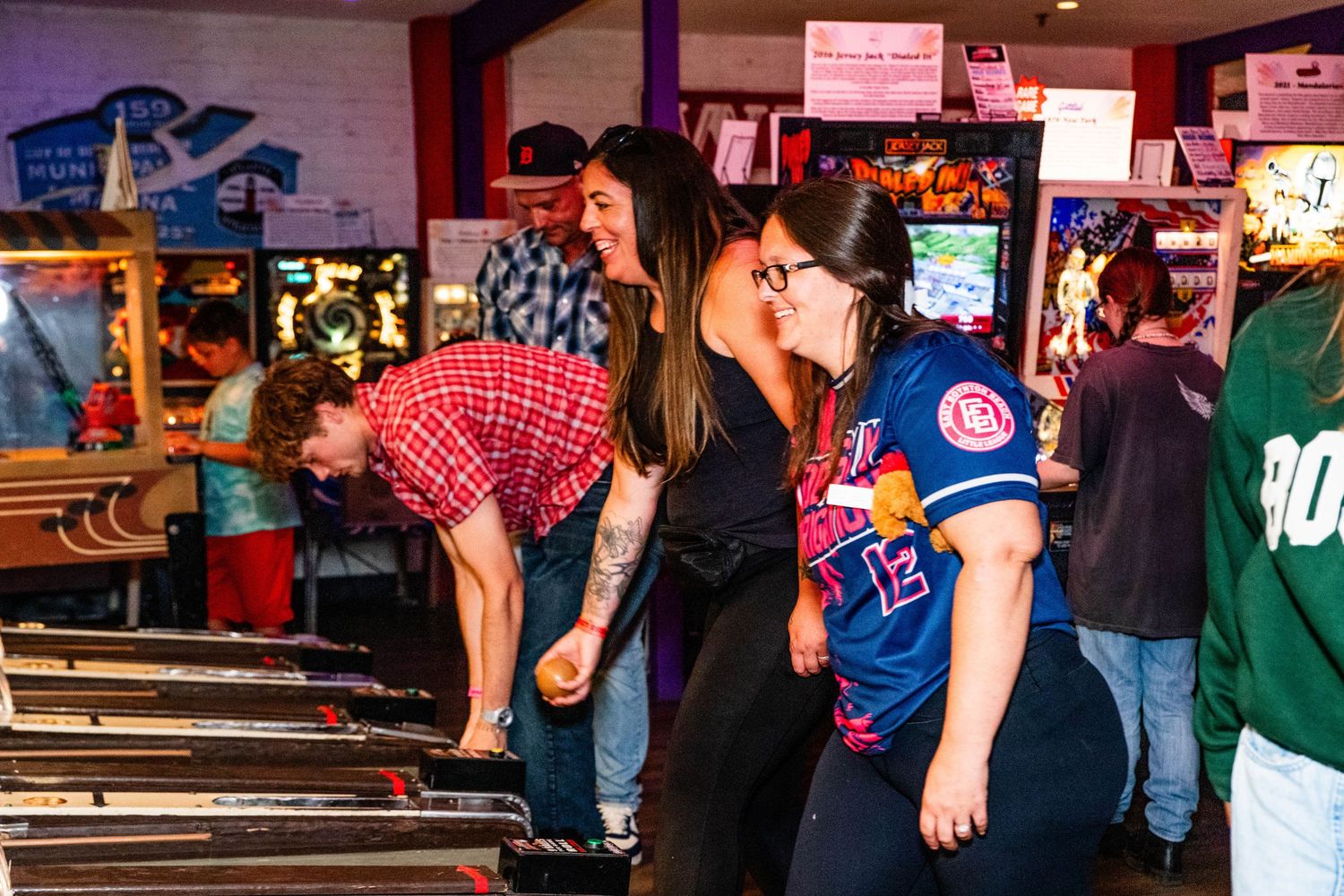 Group of friends enjoying arcade games including skee-ball at a retro gaming bar or entertainment venue.