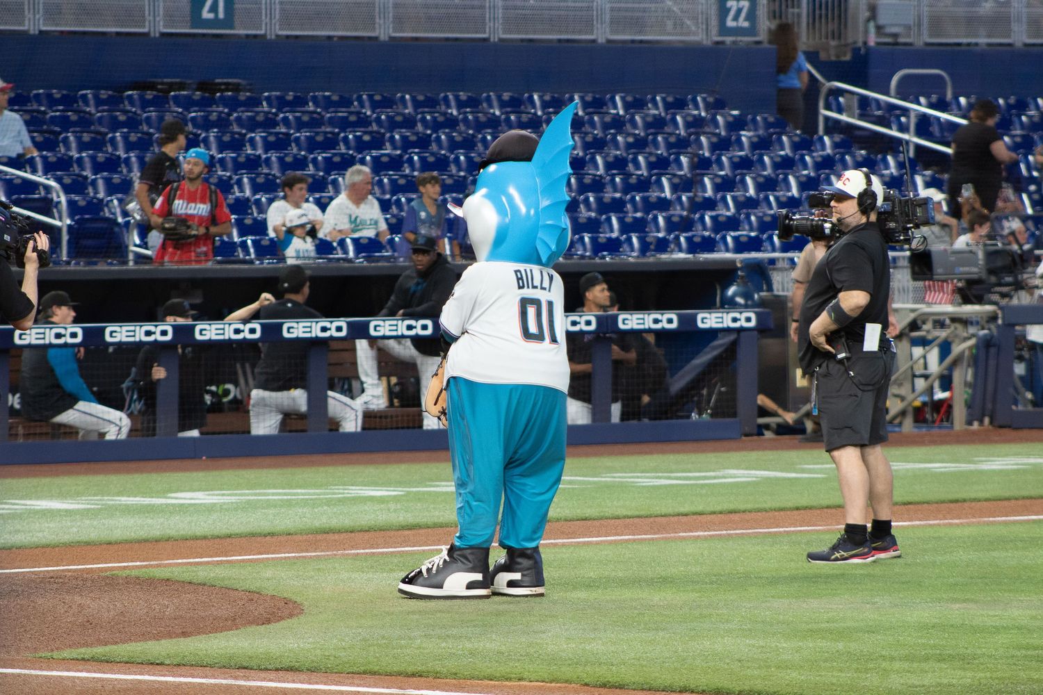 A blue mascot stands on a baseball field with empty blue stadium seats in the background.