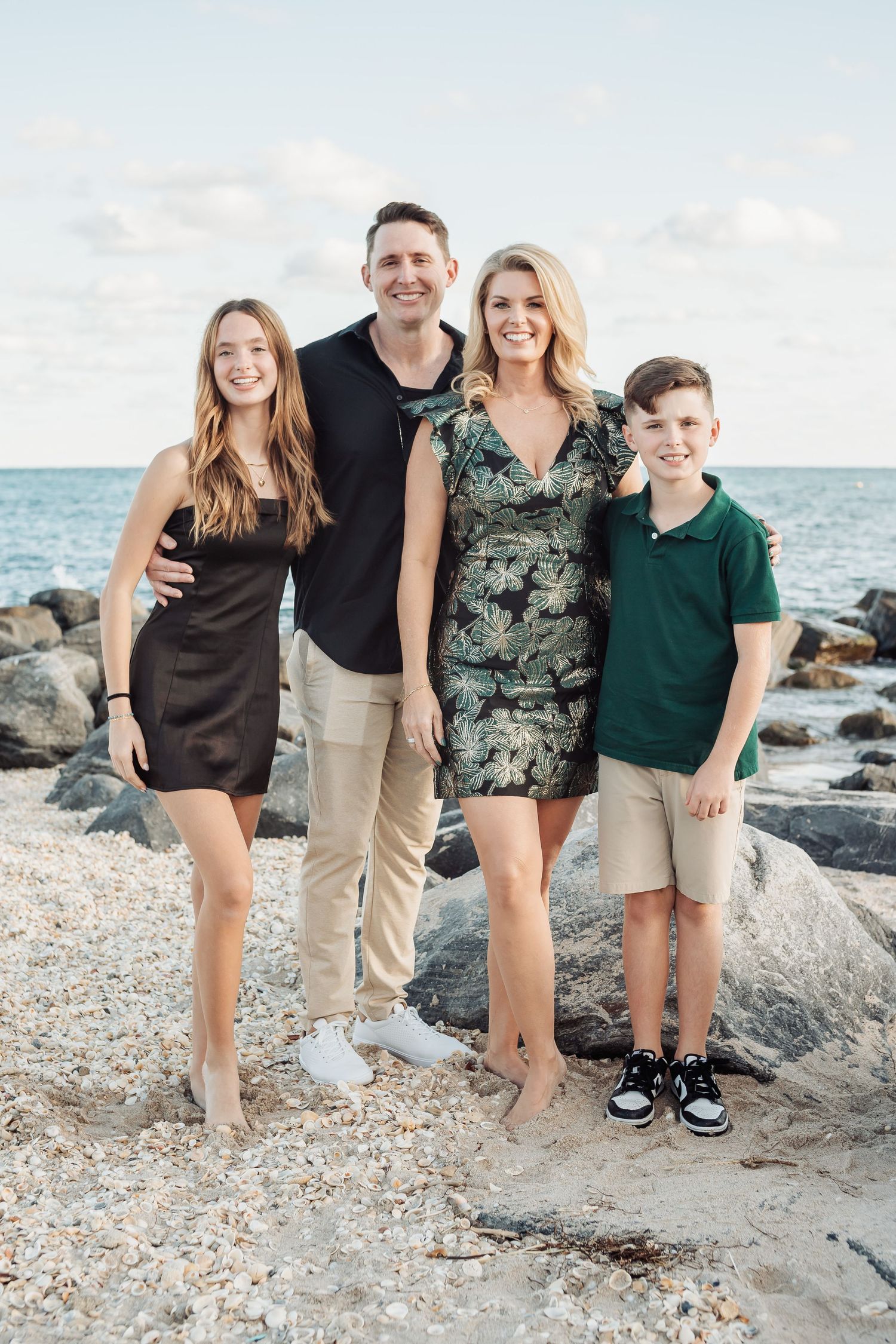 A family of four poses for a portrait on a rocky beach at sunset.