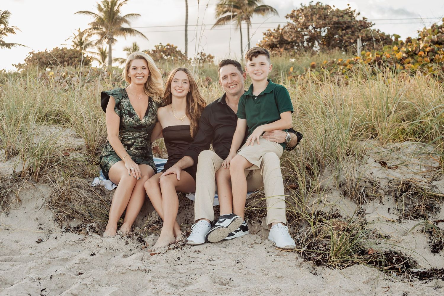 Casual family portrait session on sandy beach with tropical vegetation in background.