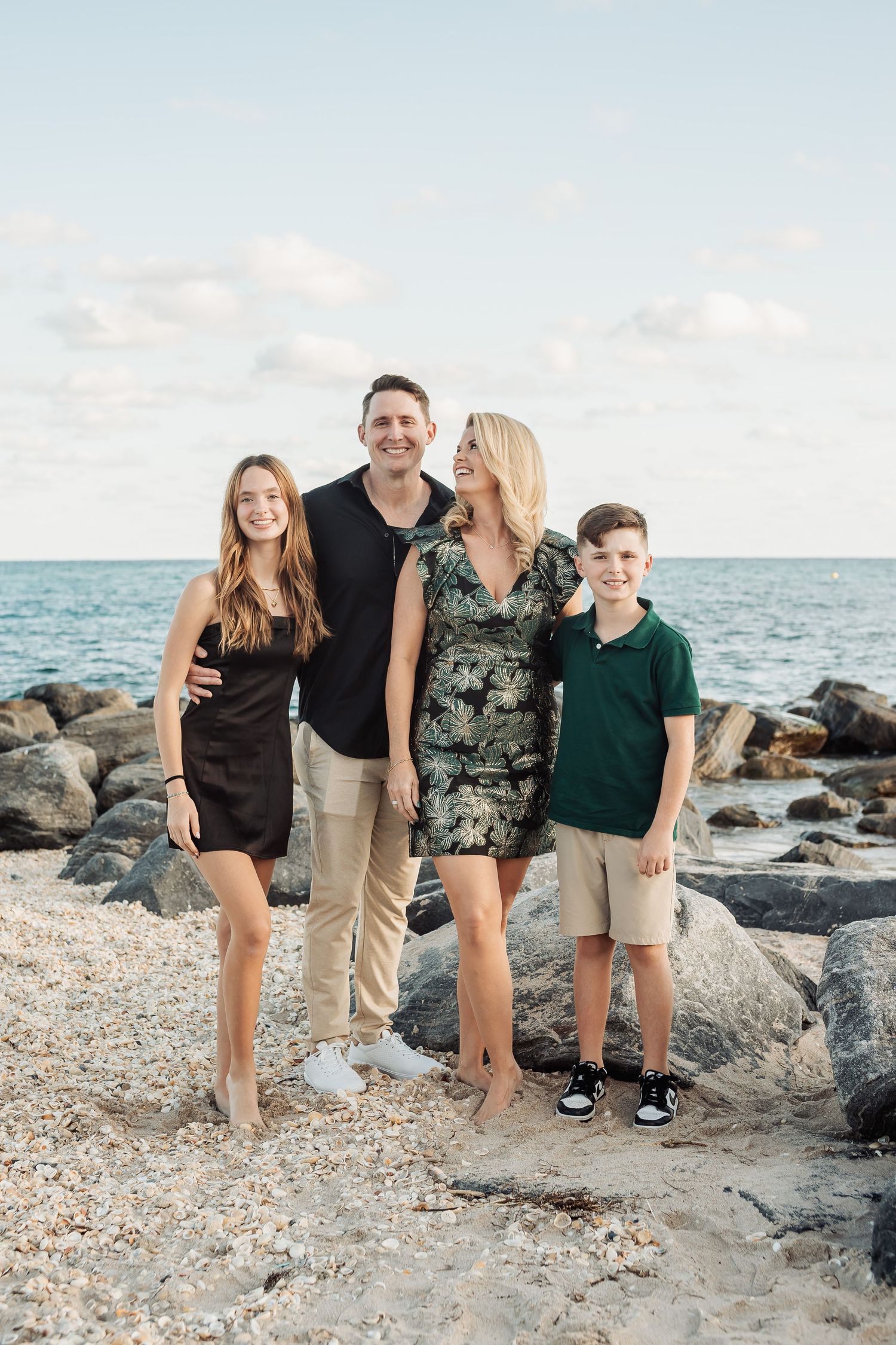 Family of four poses together on rocky beach at sunset wearing coordinated outfits.