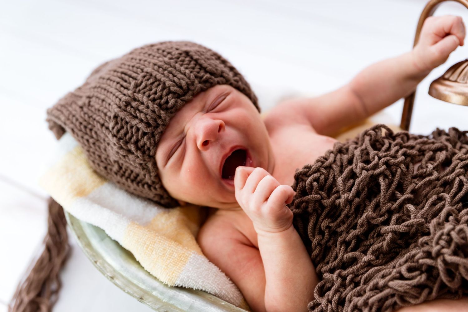 A sleeping newborn swaddled in a cozy brown knit blanket rests peacefully on white bedding.
